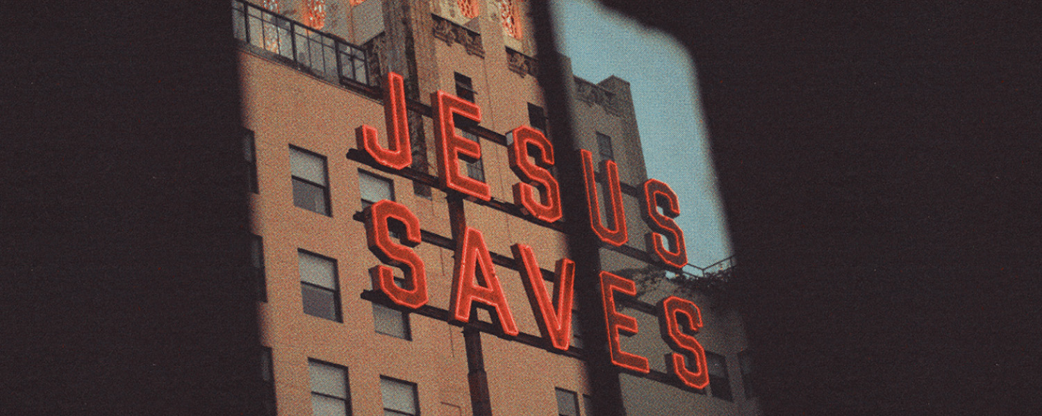 Red neon sign on building reads JESUS SAVES in bold capital letters.