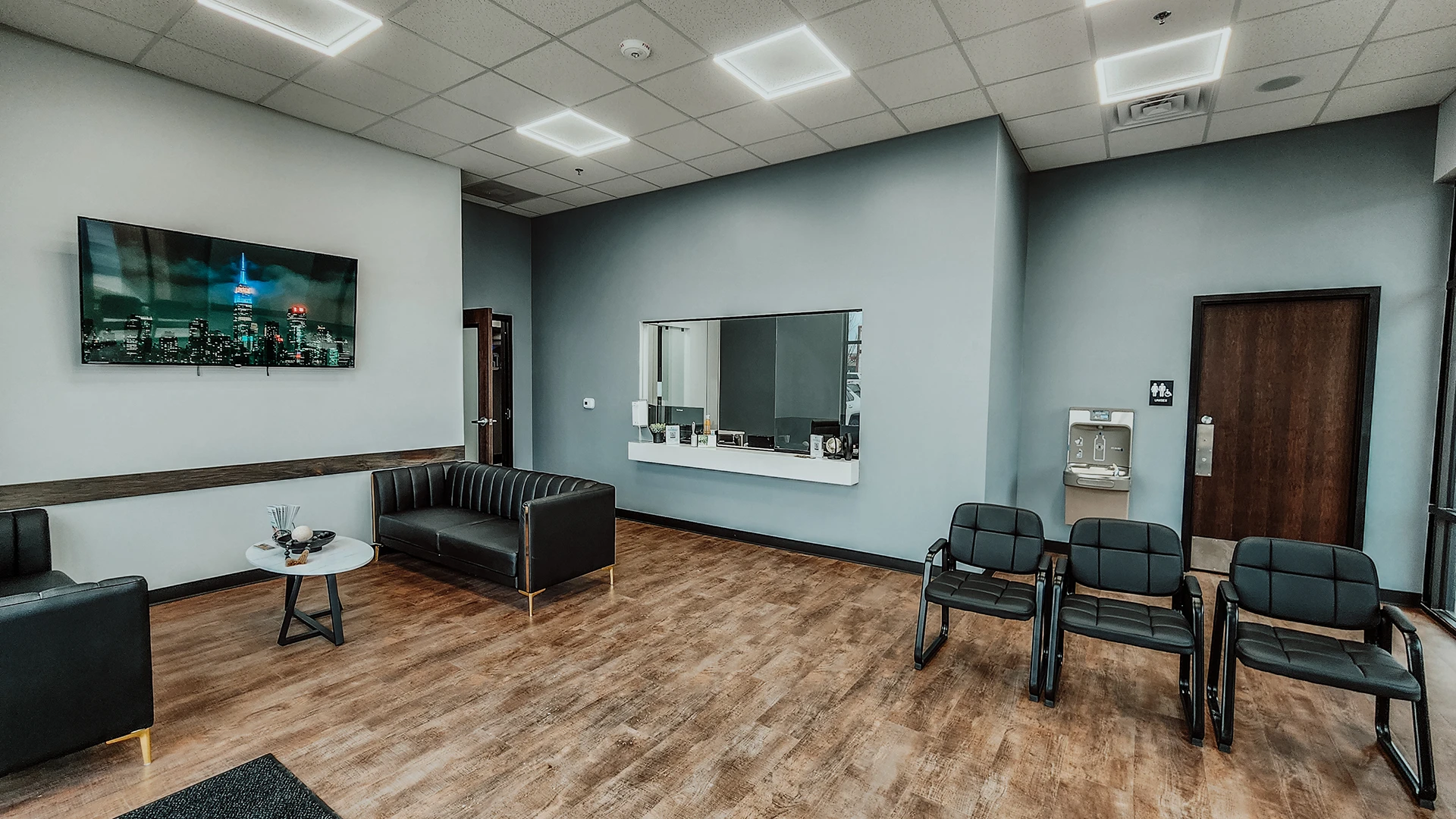 a dental lobby with wood floors and leather chairs and a tv