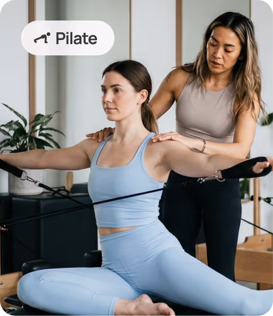 A Pilates instructor assists a woman performing a resistance exercise on a reformer machine in a studio setting.