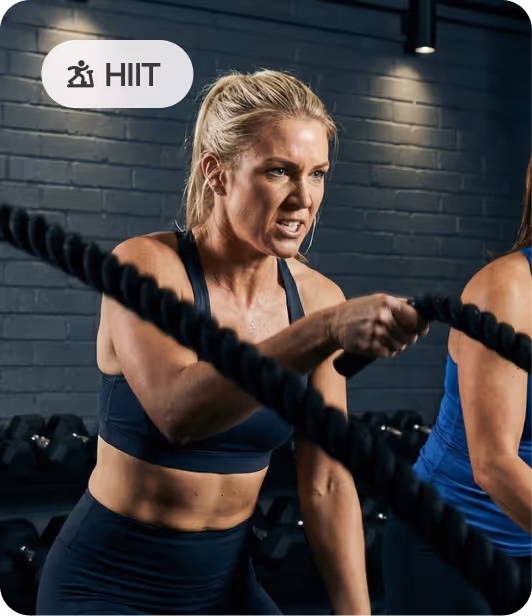 Woman intensely performing HIIT workout with battle ropes in a gym setting.