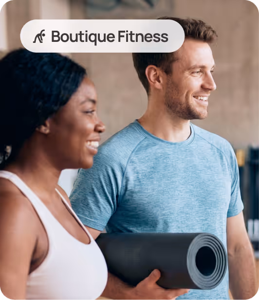 Smiling man holding a yoga mat and woman standing beside him in a fitness setting labeled Boutique Fitness.