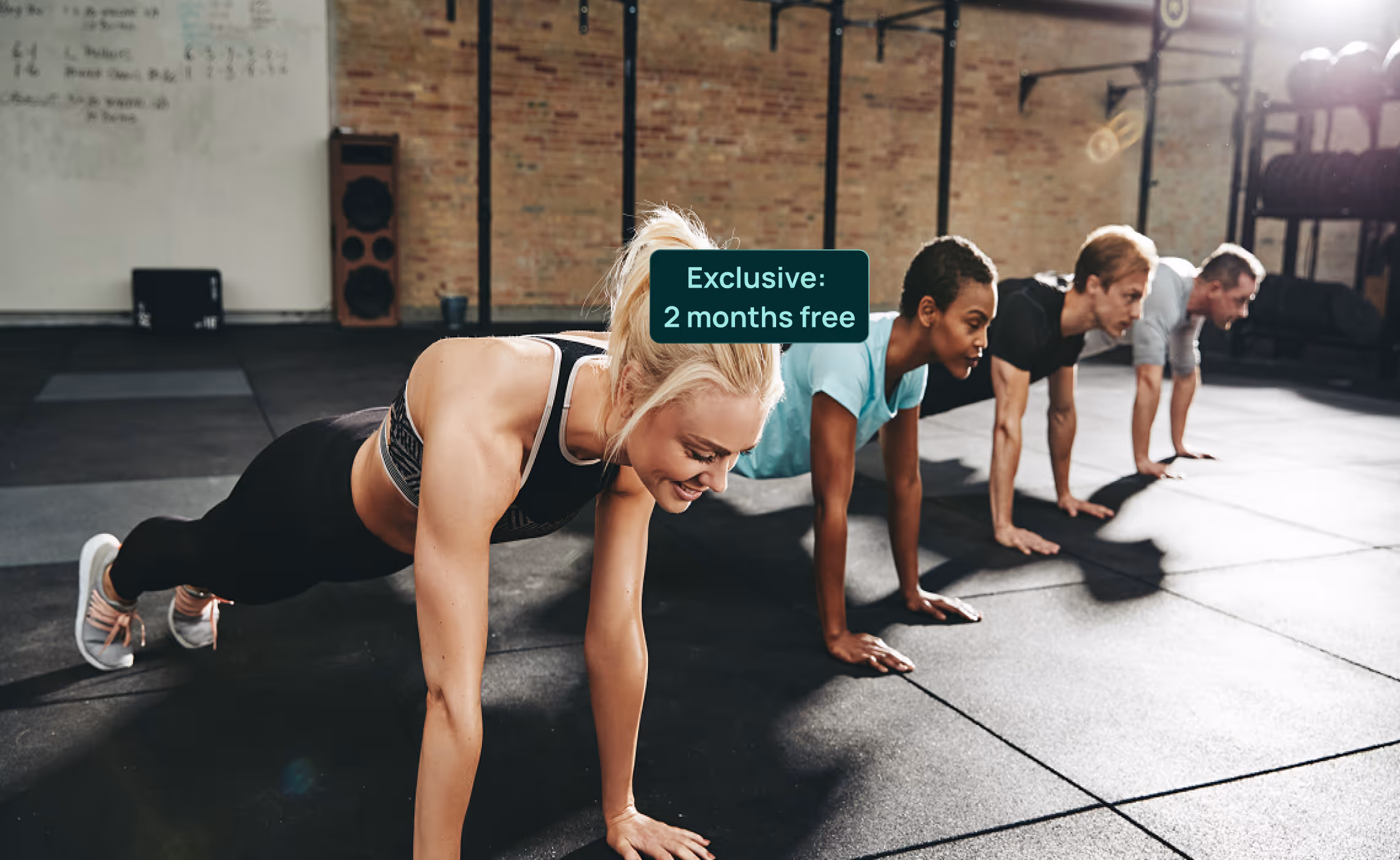 Quatre personnes dans une salle de sport en train de faire des pompes à la suite, avec un texte en surimpression indiquant « Exclusif : 2 mois gratuits ».