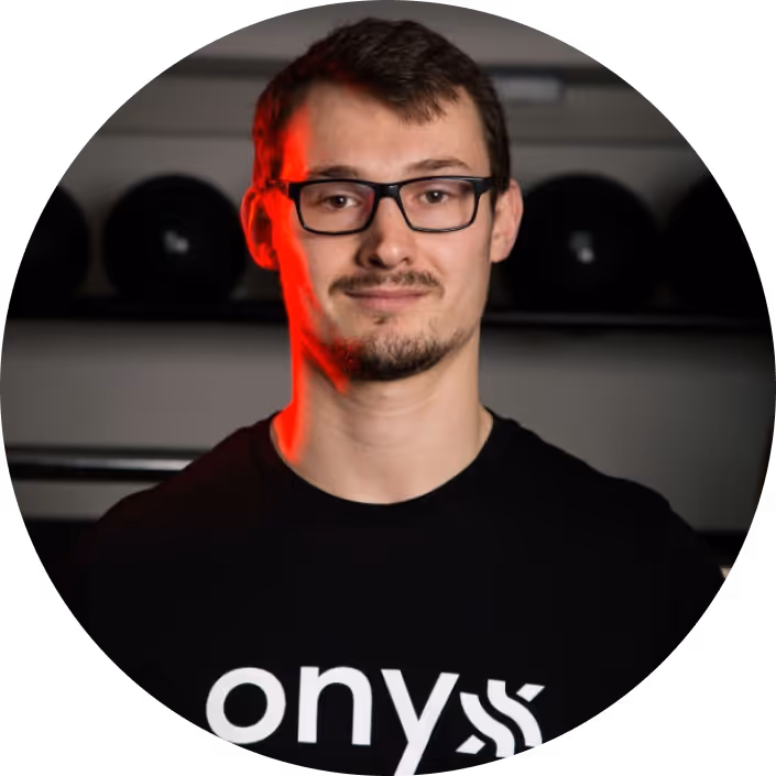 Un homme portant des lunettes et un t-shirt noir Onyx, debout devant un fond sombre, avec une lumière rouge qui éclaire un côté de son visage.