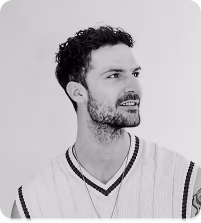 Retrato en blanco y negro de un hombre sonriente con el pelo corto y rizado, que lleva un jersey de punto sin mangas con cuello en V y un collar.