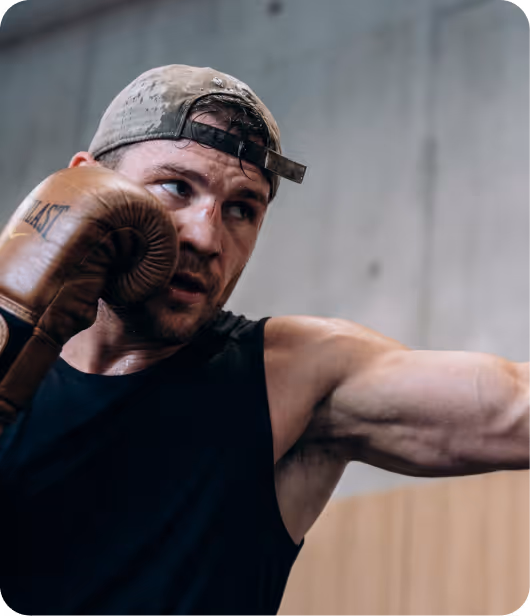 Man wearing a backwards cap and brown boxing gloves throwing a punch during a workout.