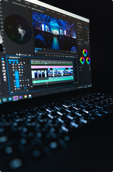 Close-up of a laptop screen showing video editing software with timeline and color correction tools, keyboard blurred in foreground.