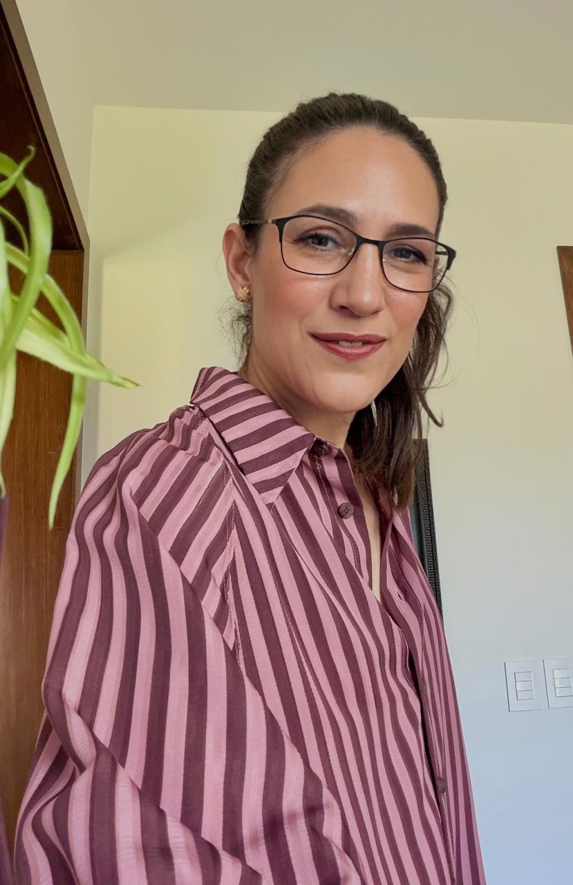 Woman wearing glasses and a pink and purple striped shirt smiling indoors.