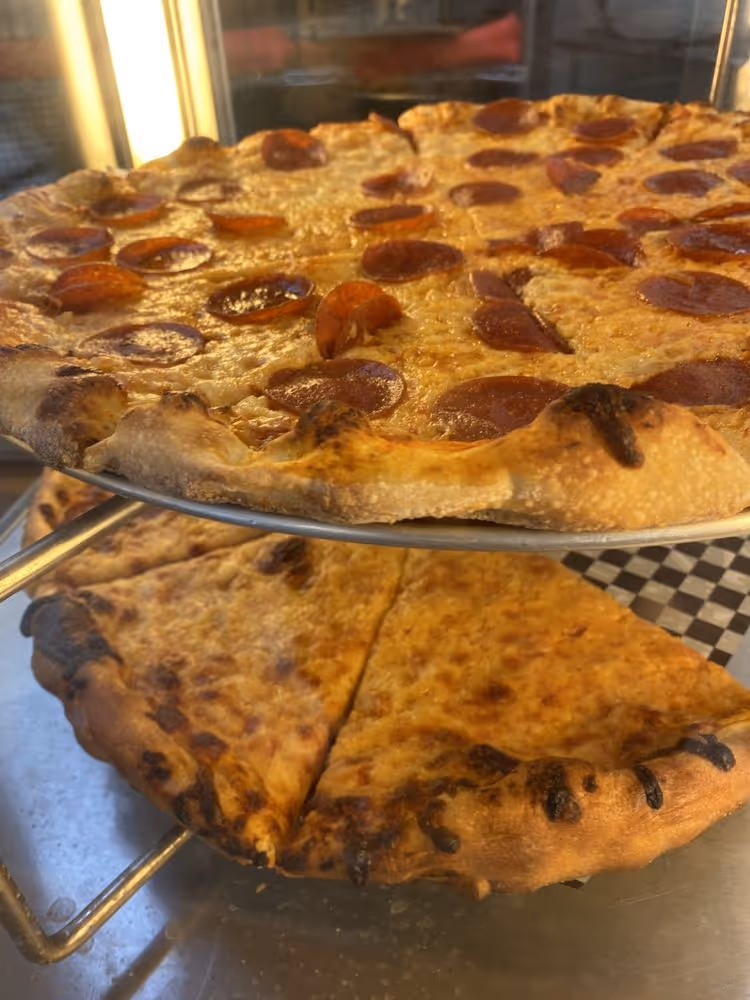 Two pizzas displayed in a pizza warmer, the top one with pepperoni toppings and the bottom one plain cheese.