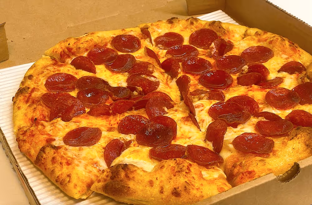 Pepperoni pizza with melted cheese in a cardboard delivery box, one slice slightly pulled out.