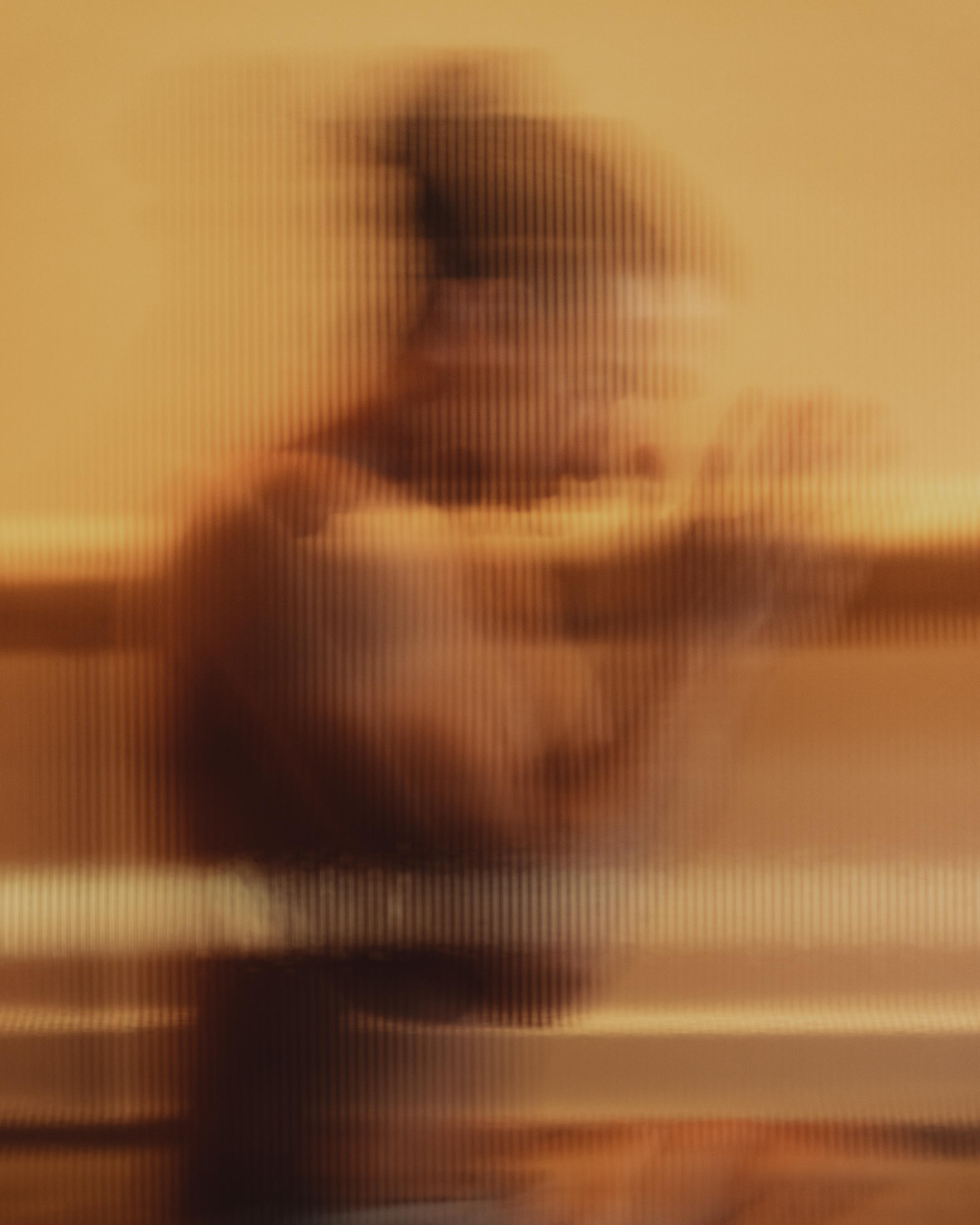 Blurred figure of a person seen through textured glass with warm golden lighting, evoking a sense of inner stillness