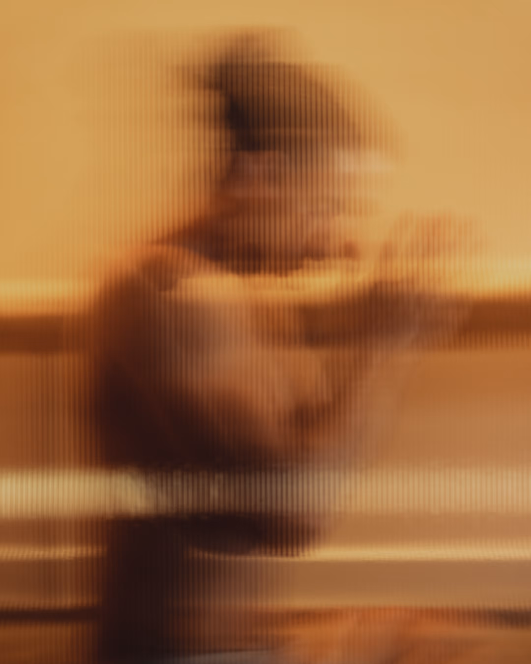 Blurred figure of a person seen through textured glass with warm golden lighting, evoking a sense of inner stillness