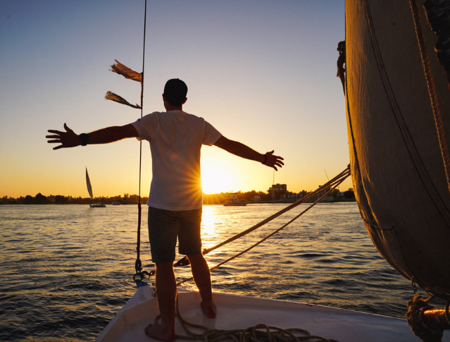 Felouque naviguant sur le Nil au coucher du soleil à Louxor, Égypte, offrant un panorama emblématique du fleuve et de ses paysages.