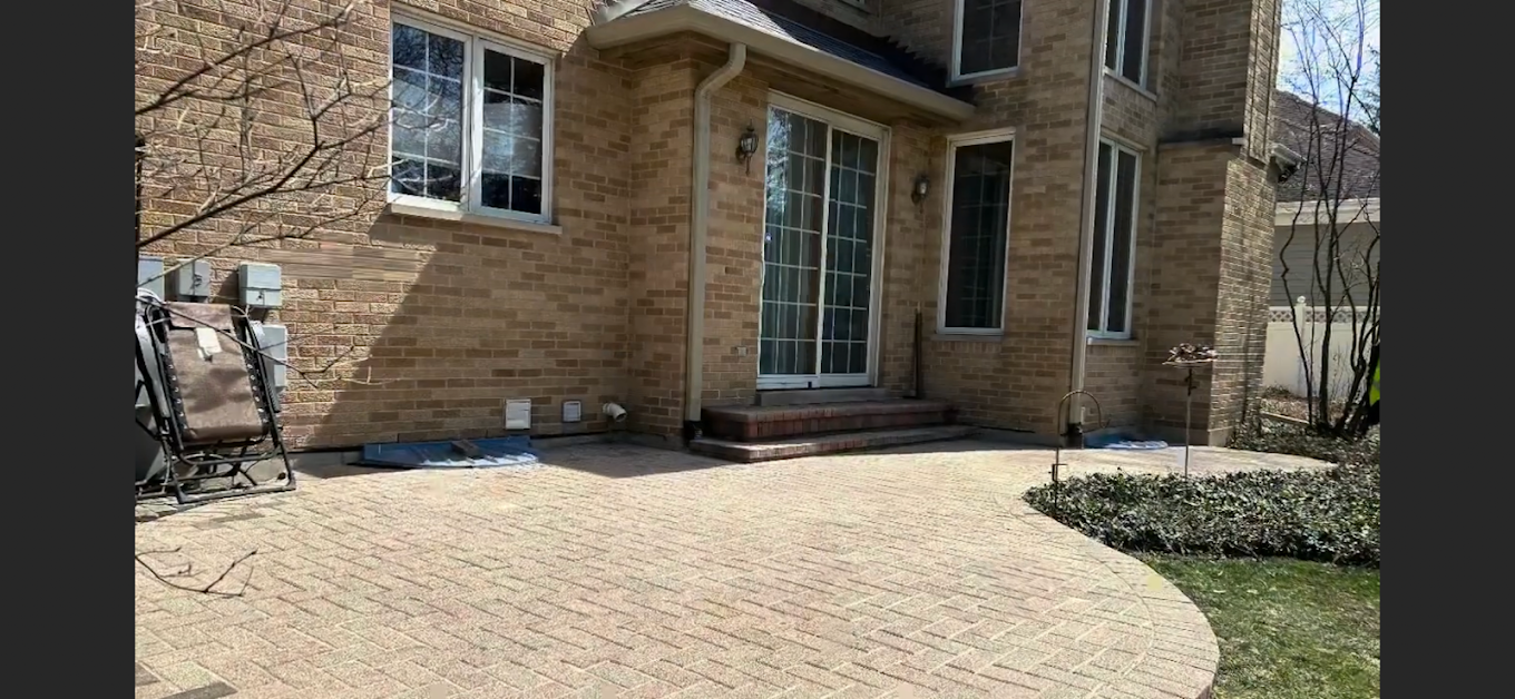 Brick patio with a curved edge next to a brick house featuring sliding glass doors and several windows.