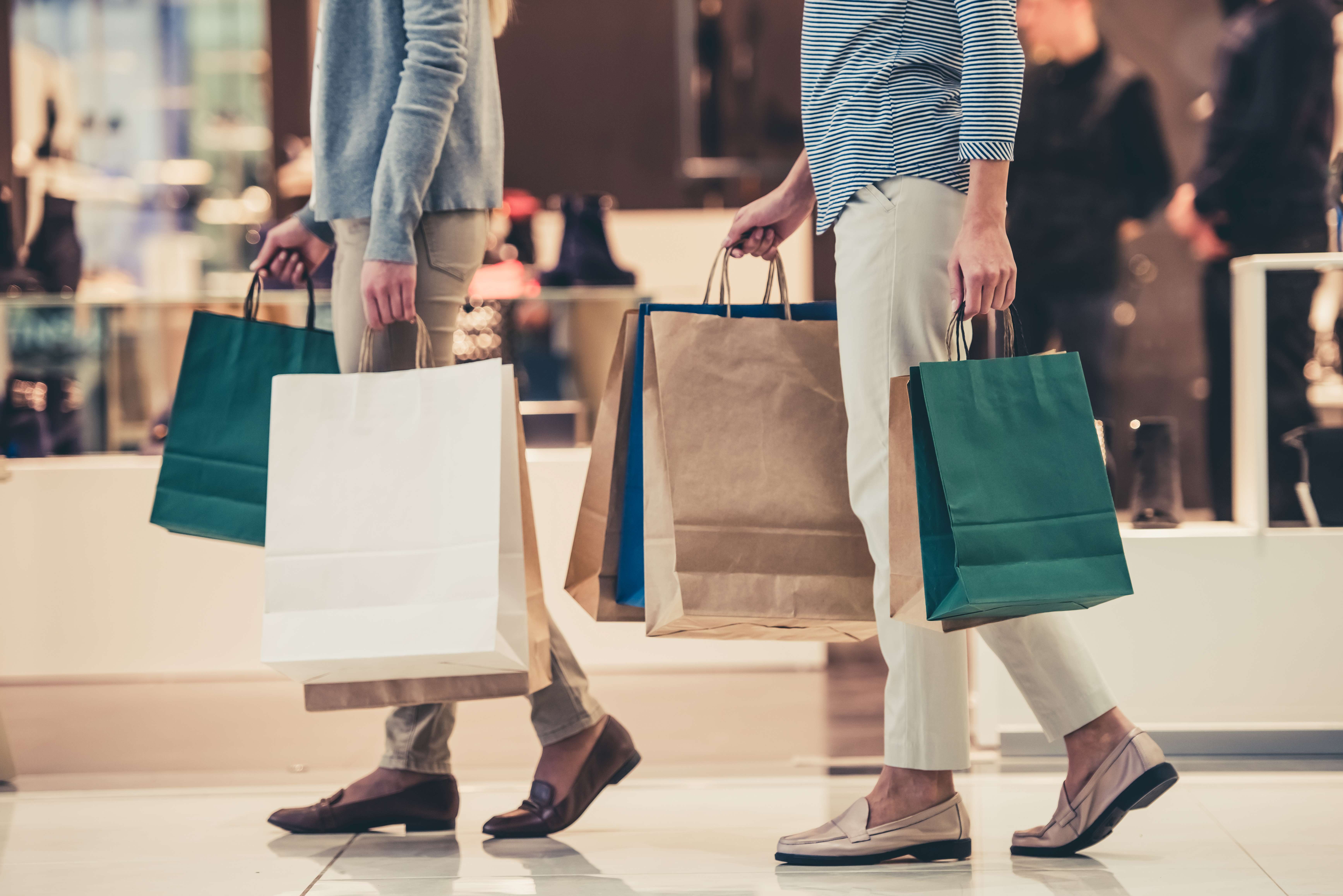Two people walking inside a store carrying multiple shopping bags in their hands.