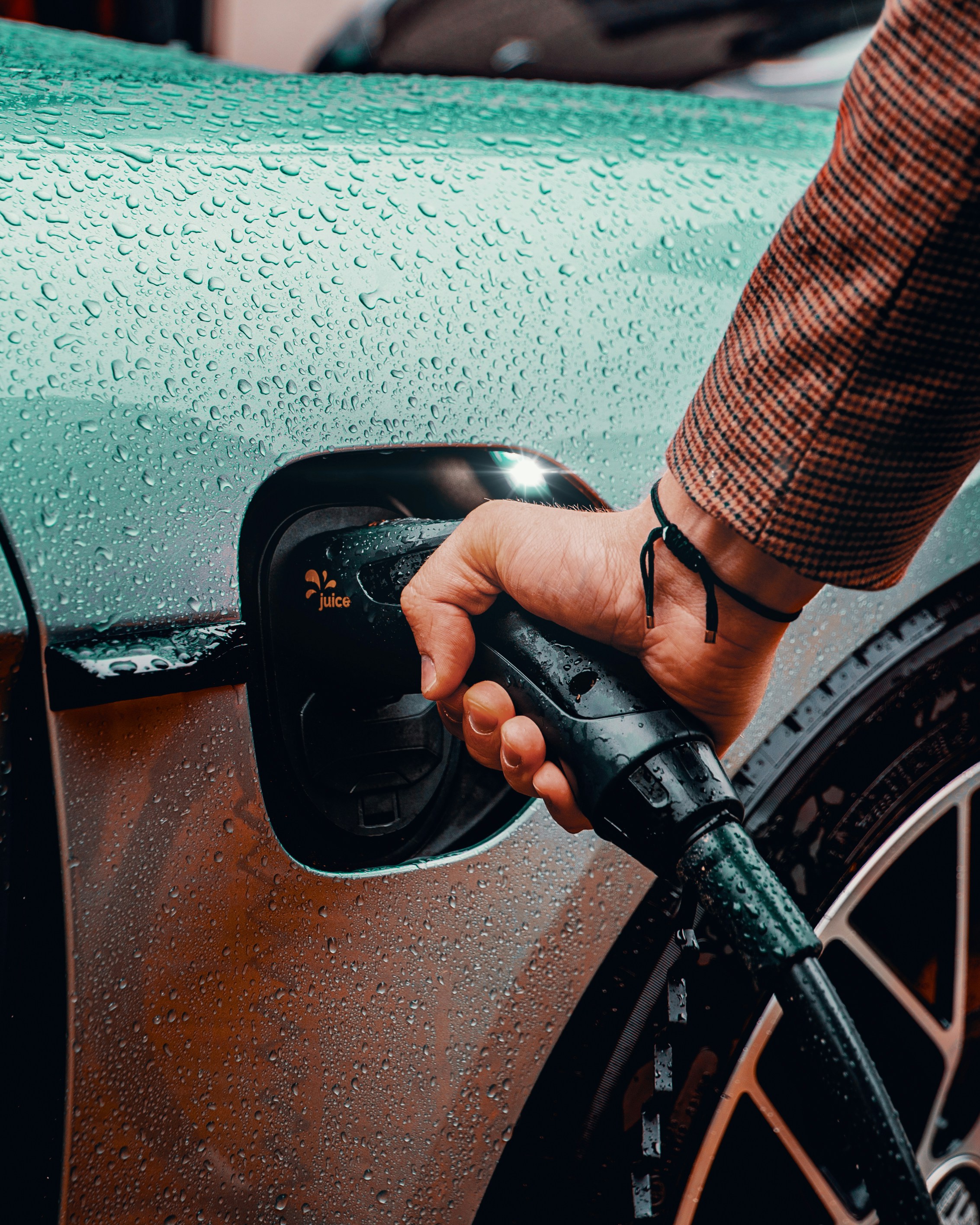 Hand plugging a charging cable into a rain-covered electric vehicle.