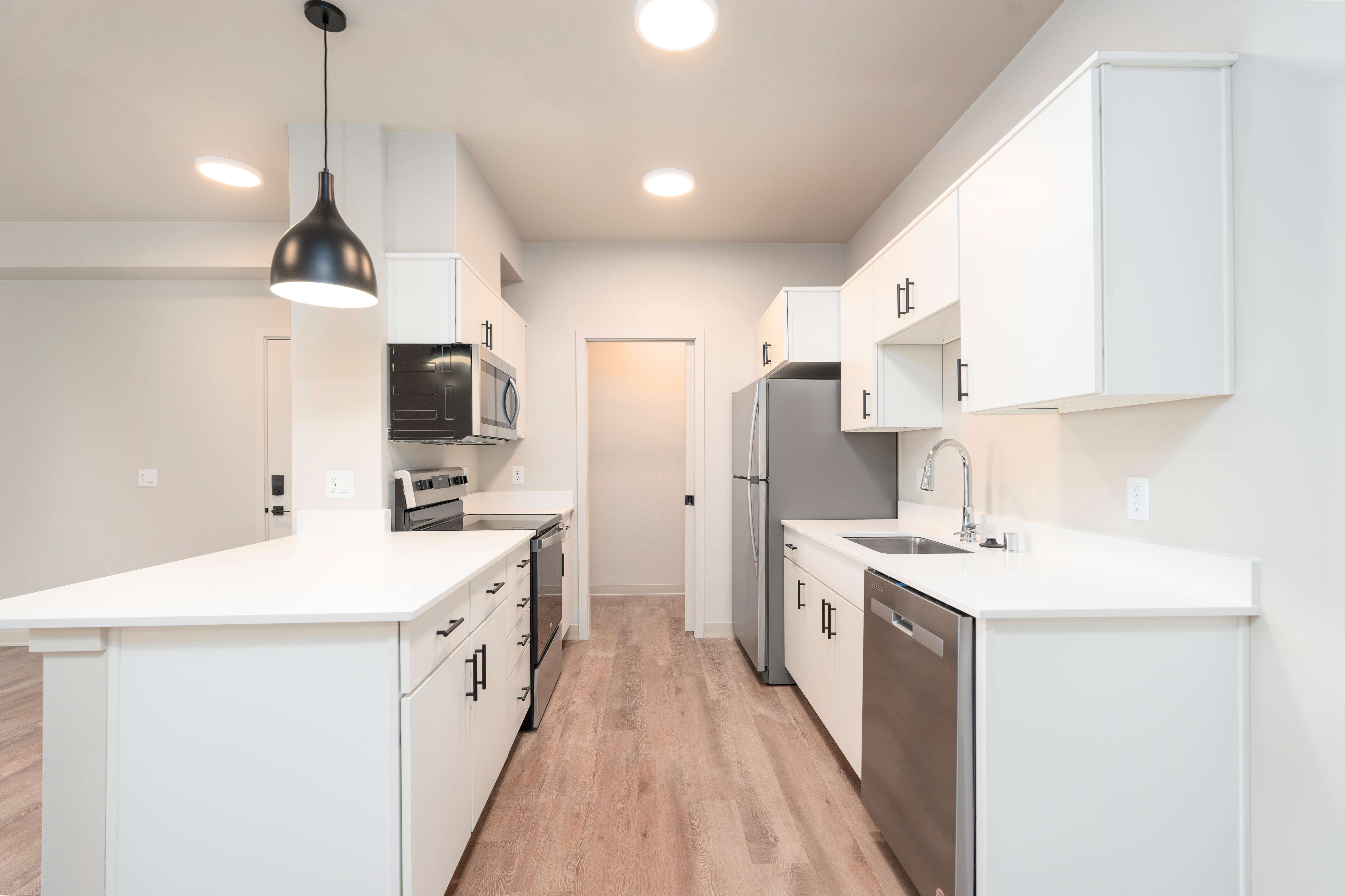 Modern kitchen with white cabinets, stainless steel appliances, wooden floor, and black hanging light fixture.