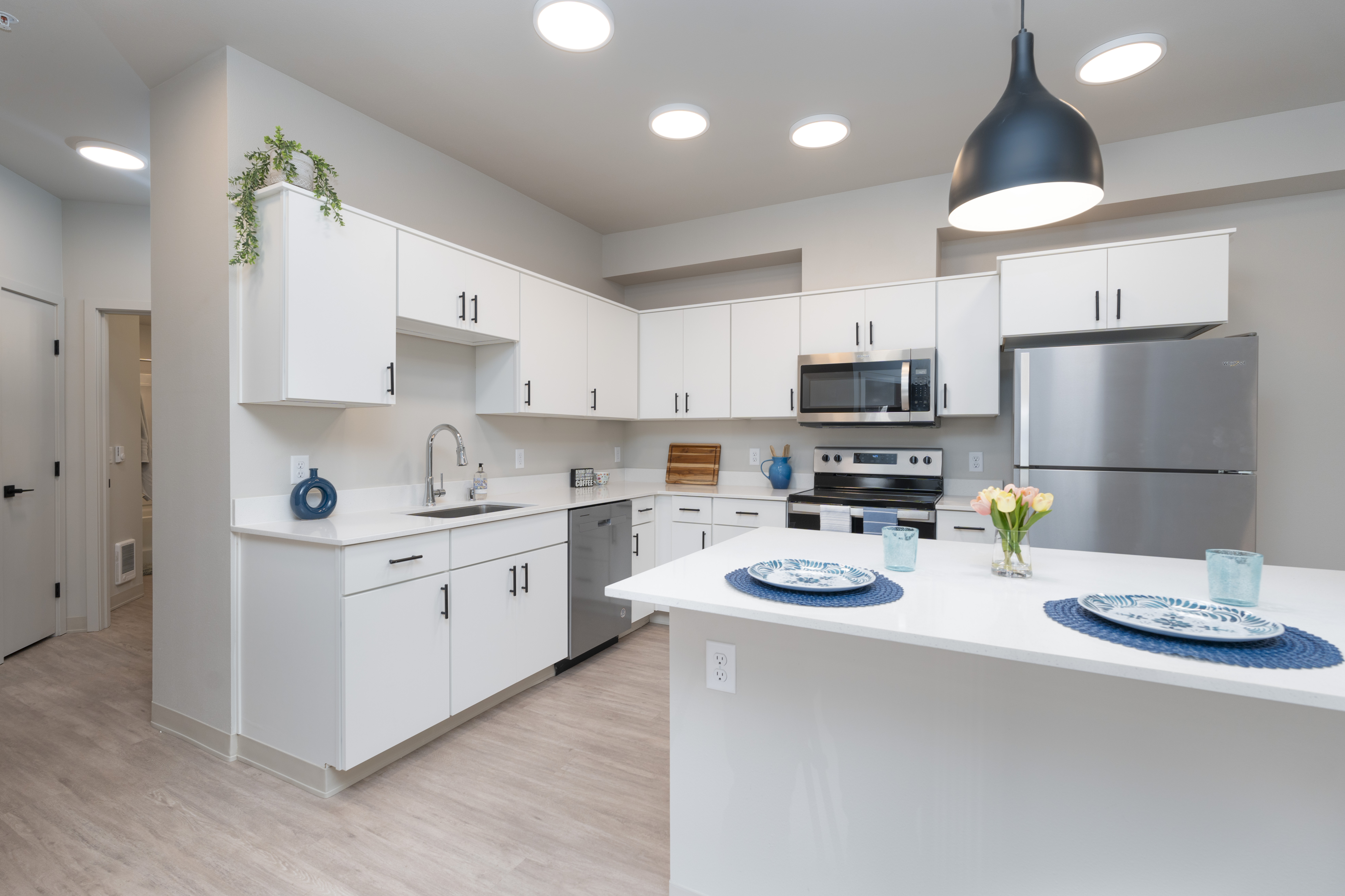 Modern kitchen with white cabinets, stainless steel appliances, island with place settings and tulip flowers, and overhead lighting.