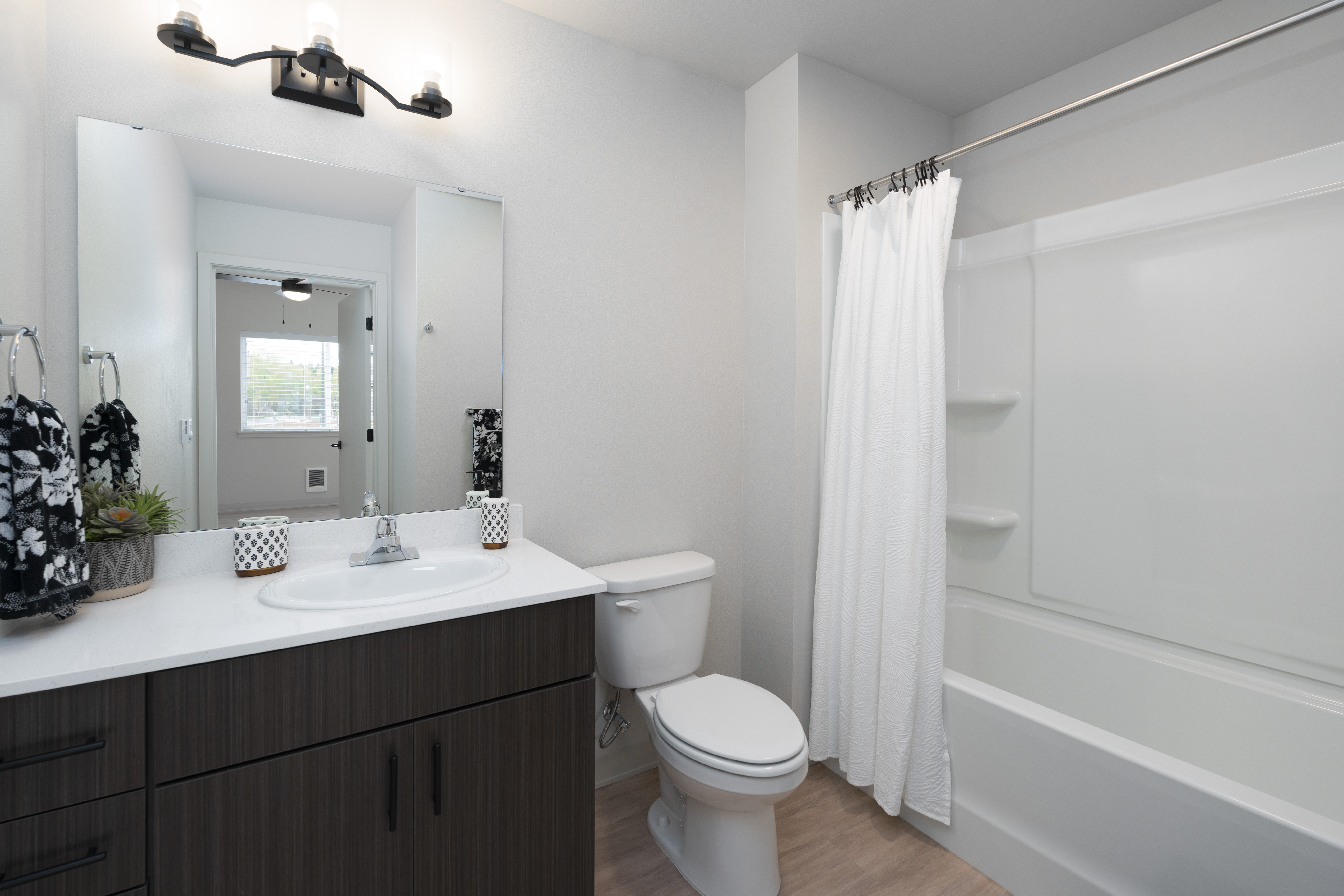 Modern bathroom with dark wood vanity, white sink, toilet, and bathtub with white shower curtain.