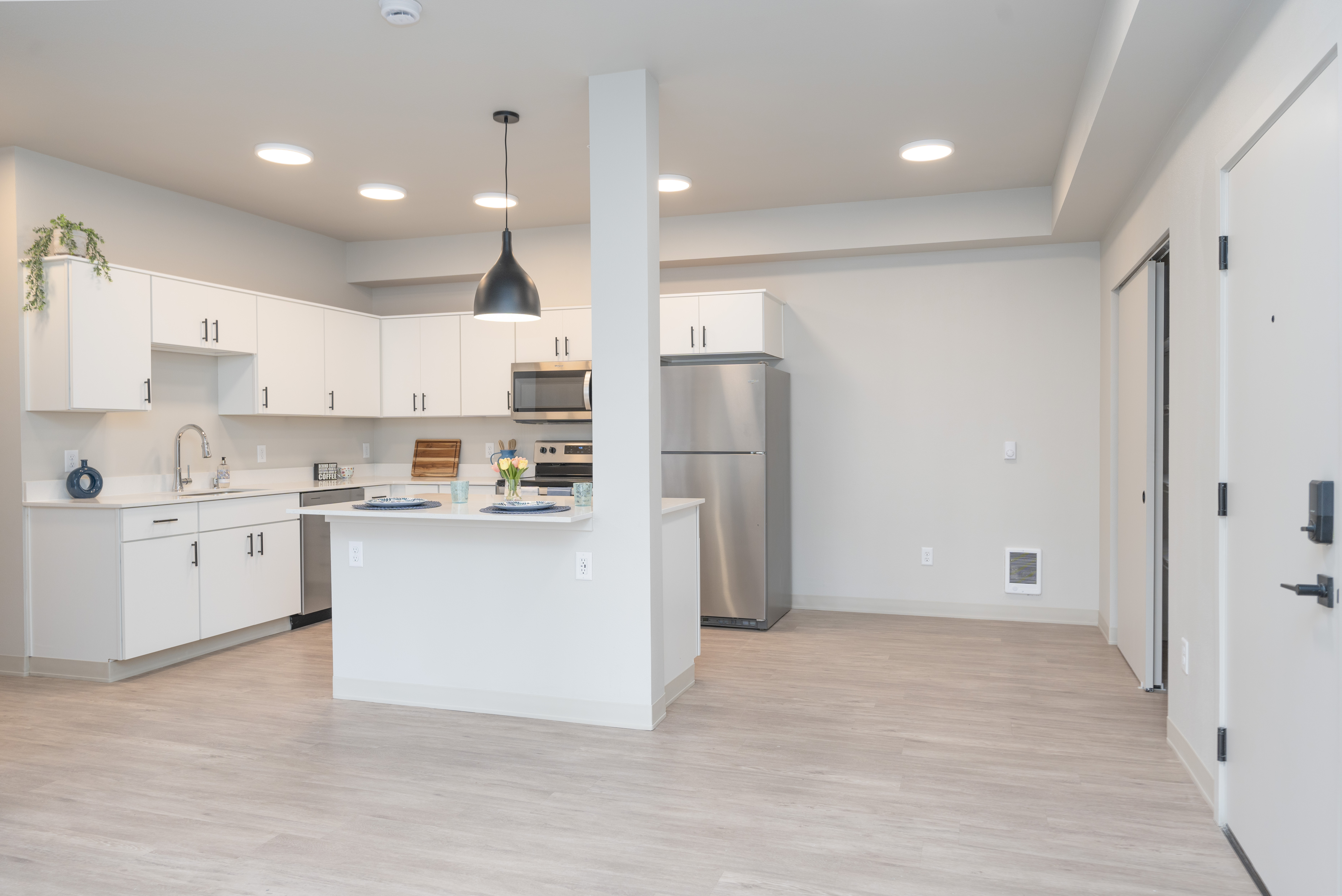 Modern kitchen with white cabinets, stainless steel appliances, an island with place settings, and light wood flooring.