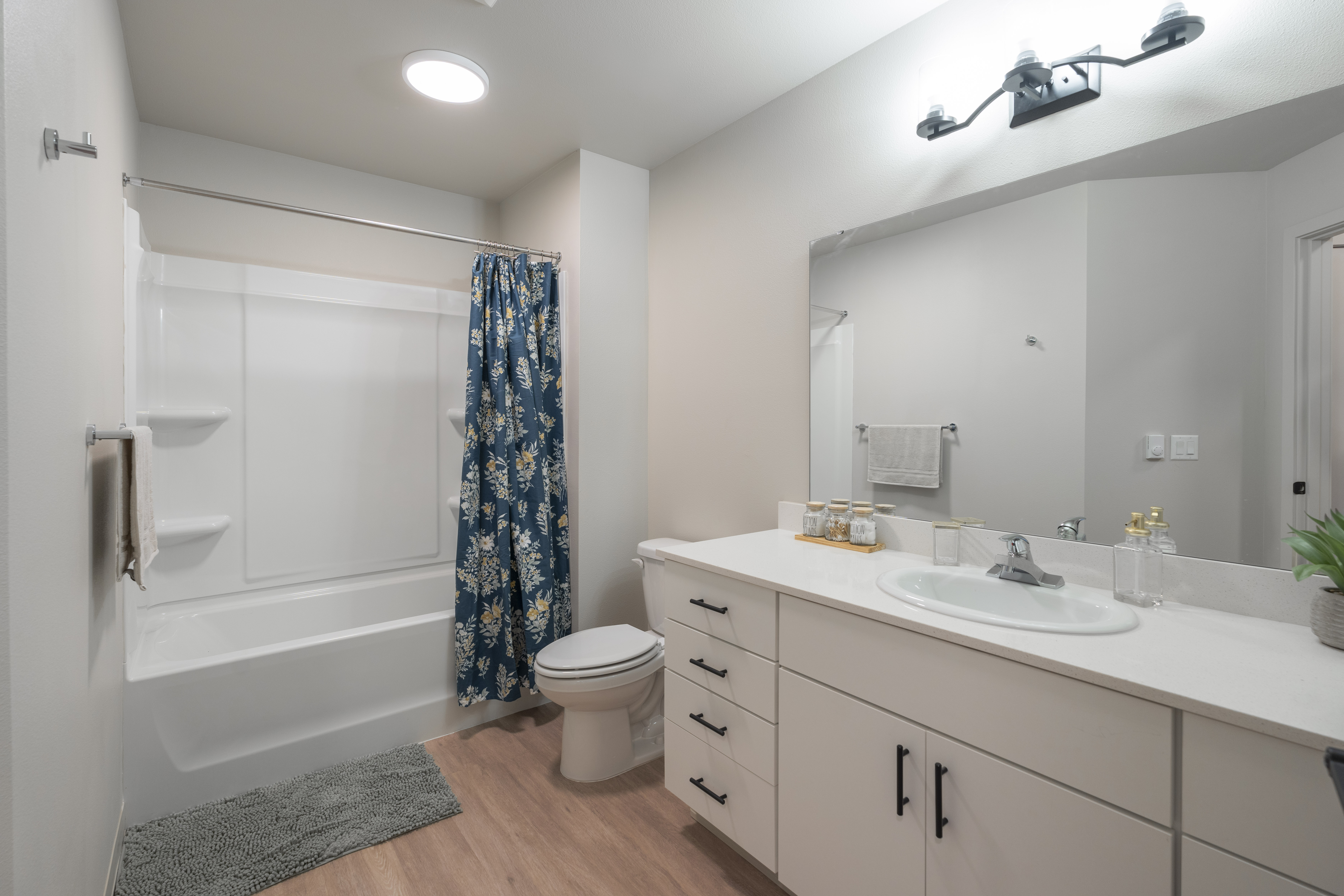 Bright bathroom with white bathtub, blue floral shower curtain, white vanity with sink, and large mirror.