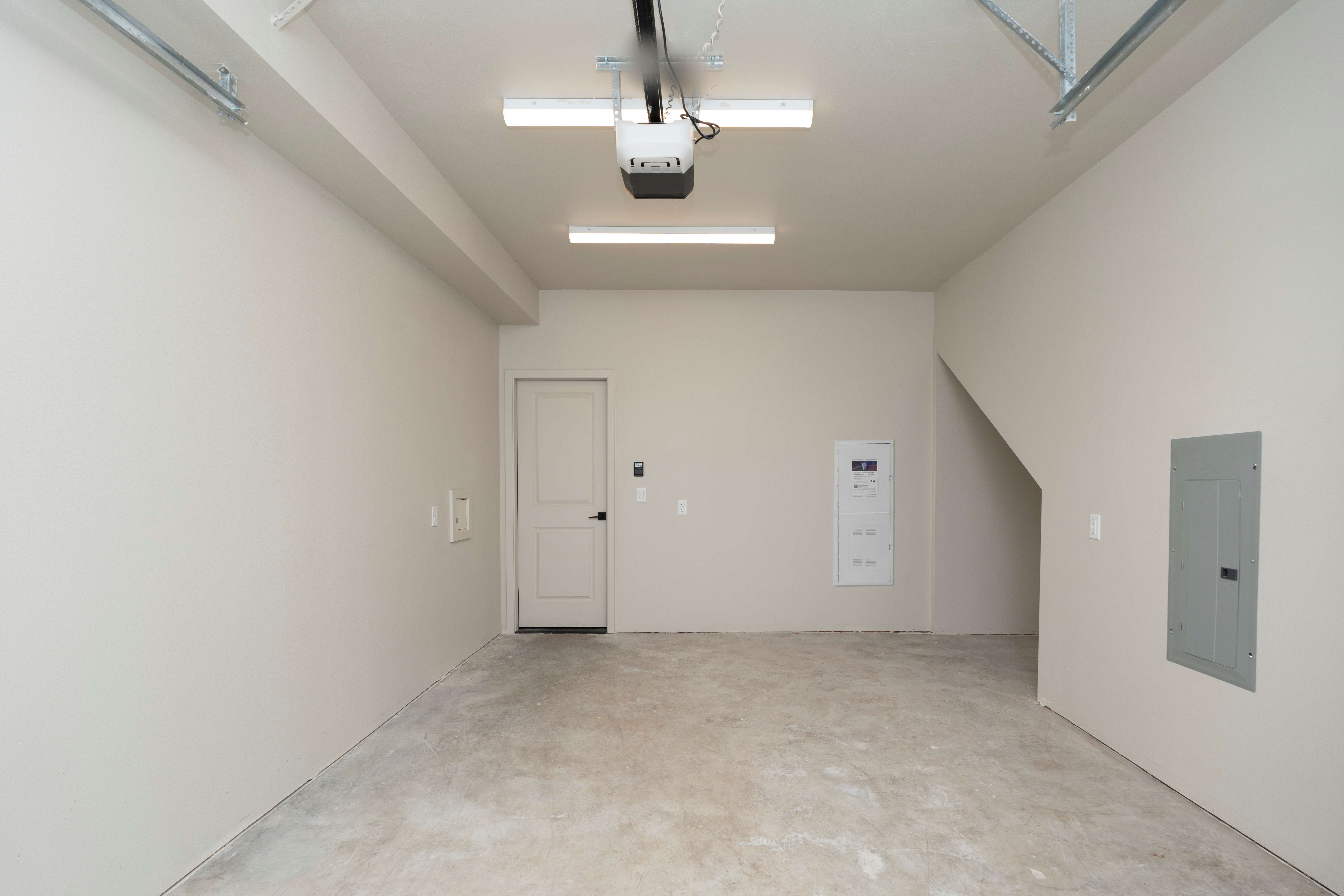 Empty clean garage with white walls, concrete floor, ceiling lights, and a closed white door at the back.