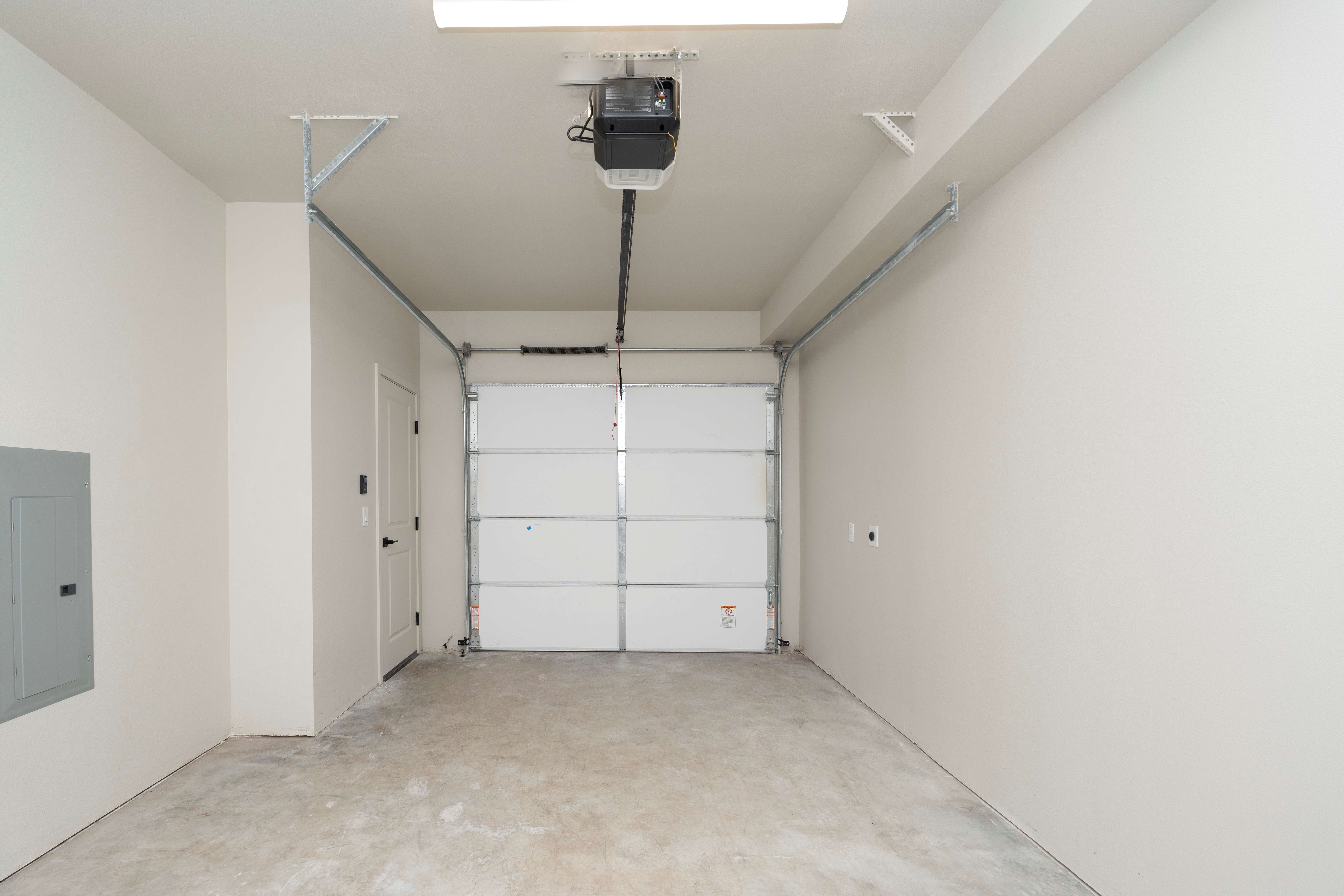 Empty residential garage with light beige walls, concrete floor, closed white sectional garage door, and ceiling-mounted garage door opener.