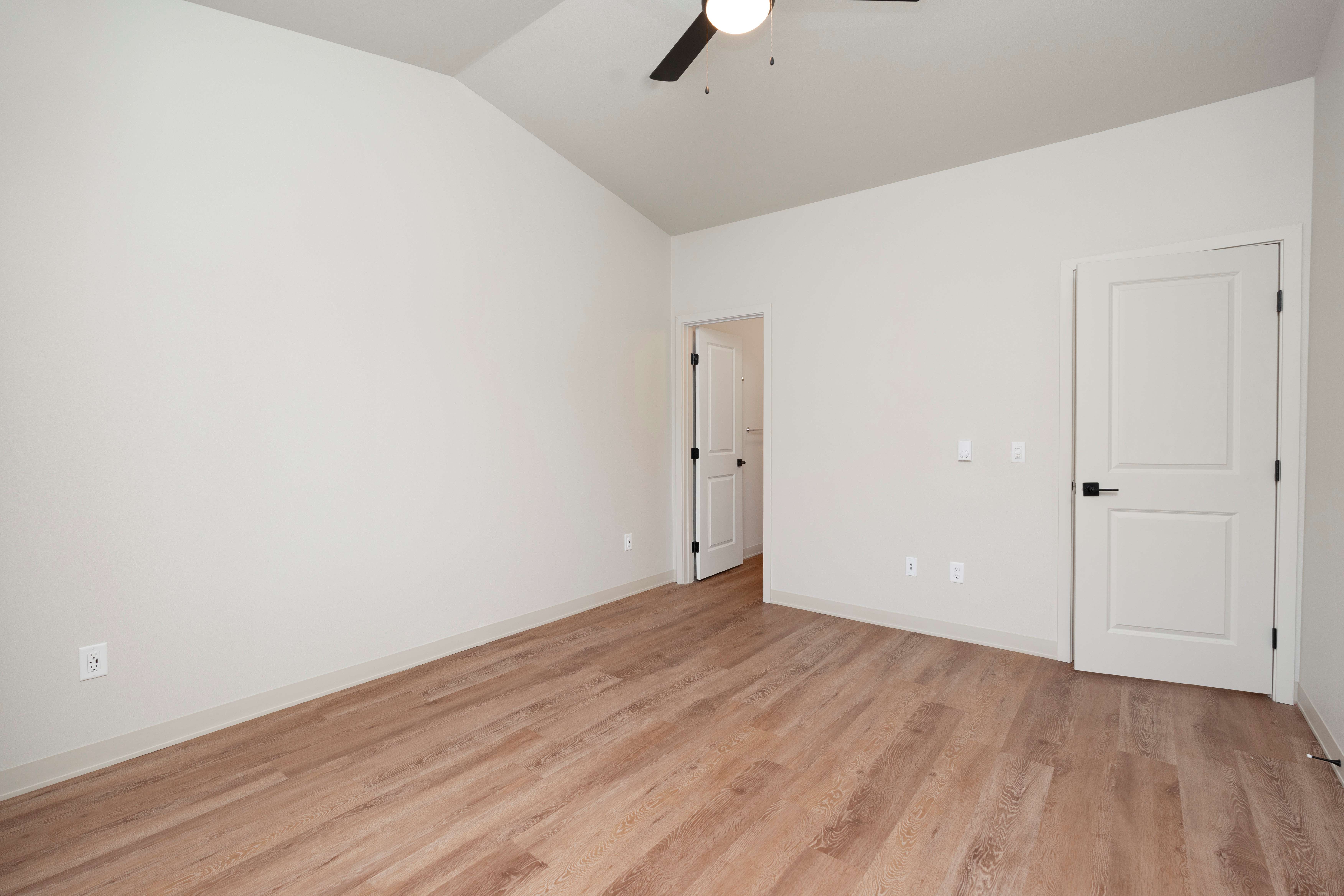 Empty room with light-colored walls, wood flooring, ceiling fan, and two white doors.
