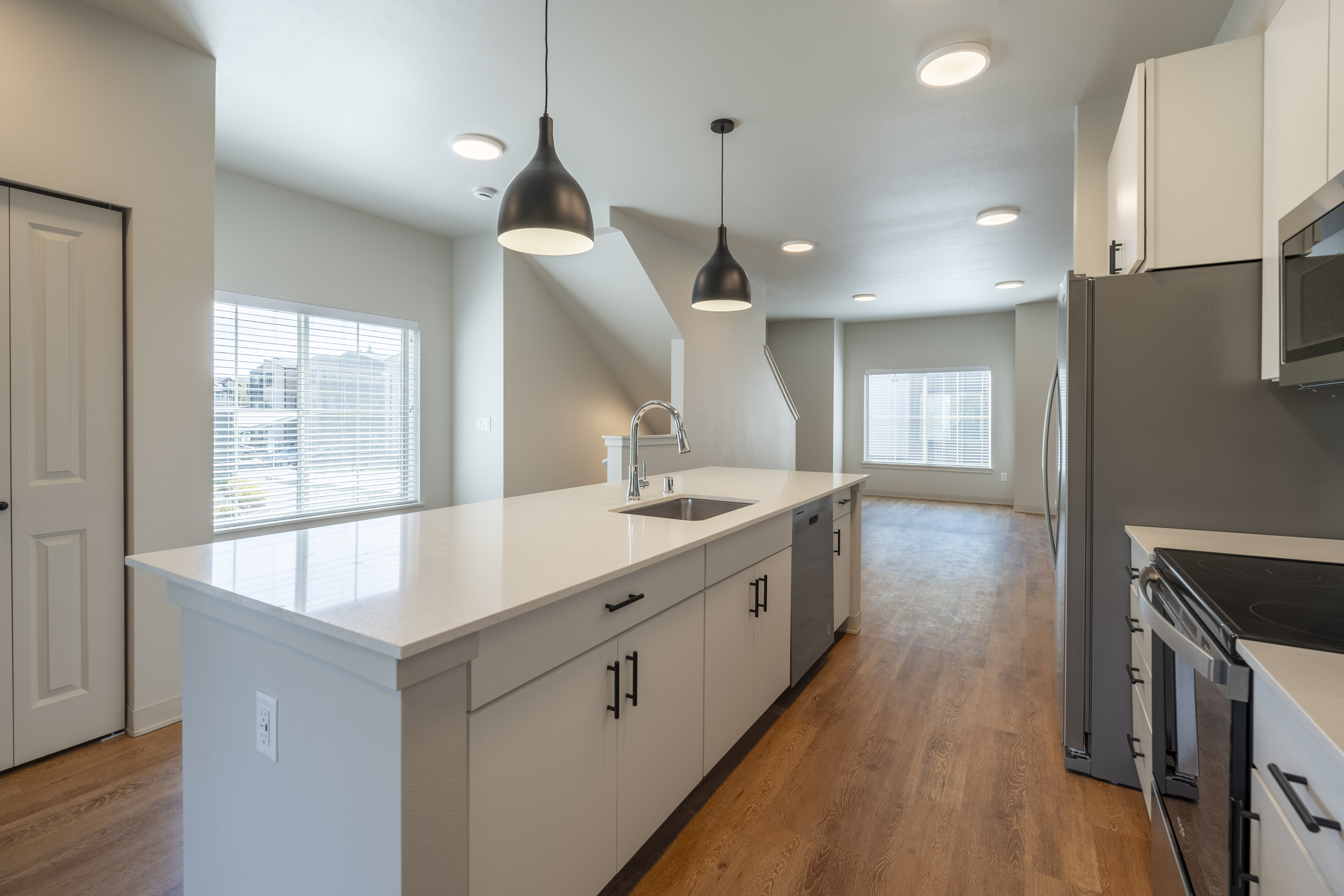 Modern kitchen with white cabinets, large island with sink, stainless steel appliances, and wooden flooring.