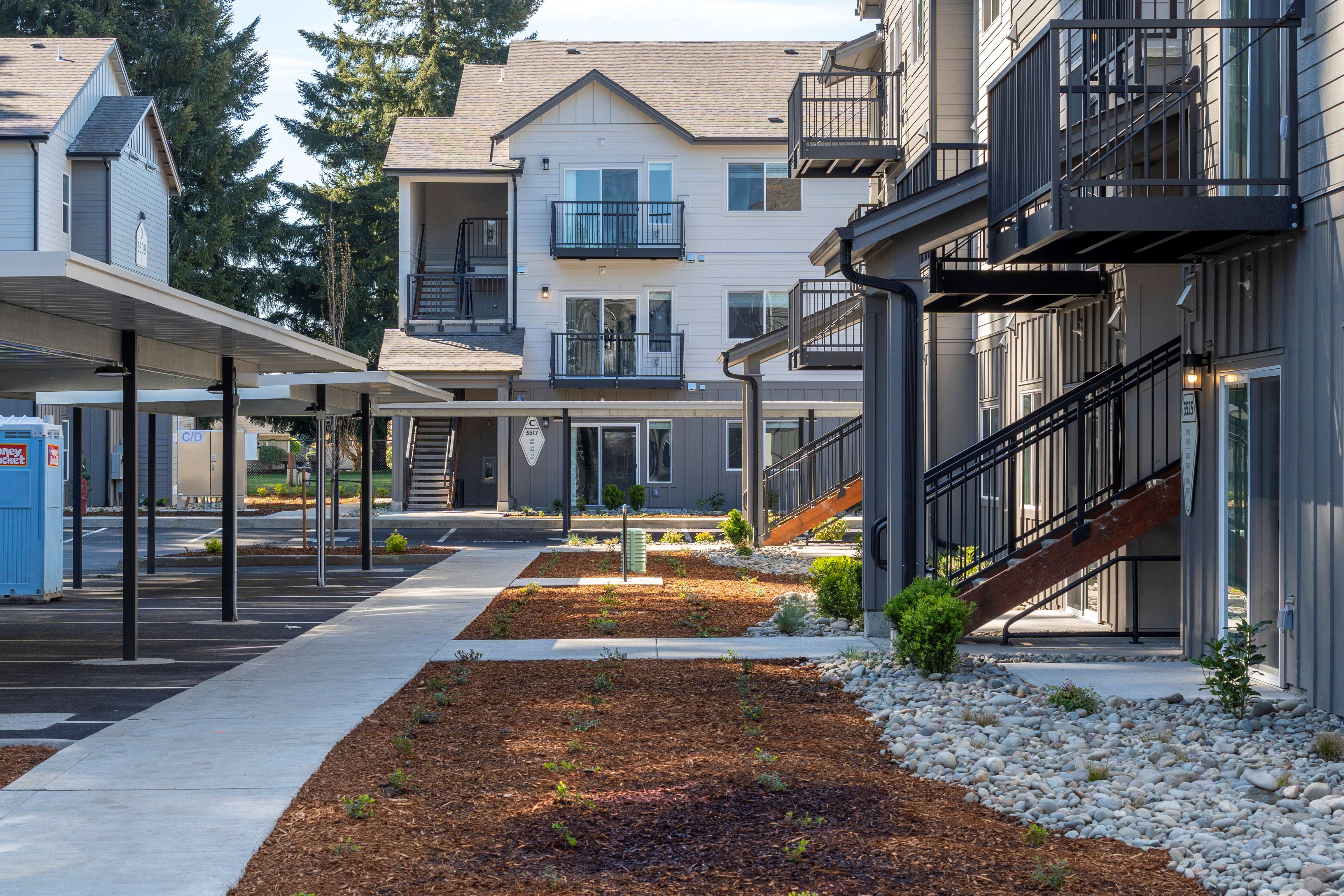Modern apartment complex with covered parking, exterior staircases, balconies, and landscaped walking paths.