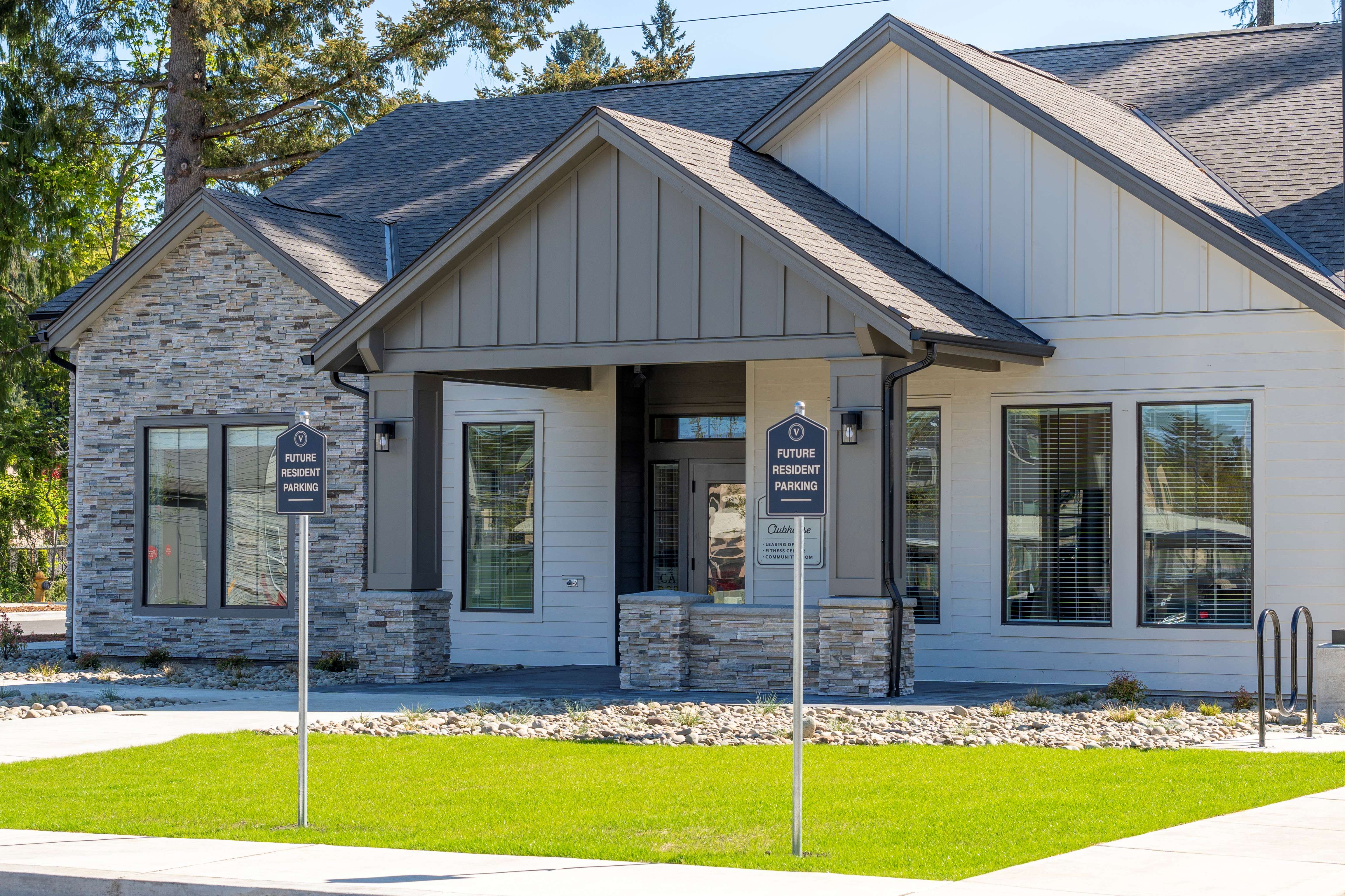 Modern clubhouse building with stone and white siding exterior and two future resident parking signs on a lawn.