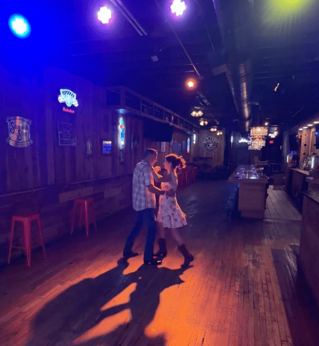 Couple dancing together under colorful lights inside a rustic bar img