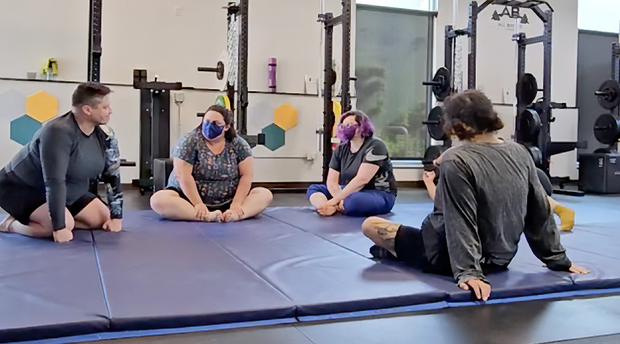 Group of people sitting on a mat during a self defense class watching Coach Shelby.