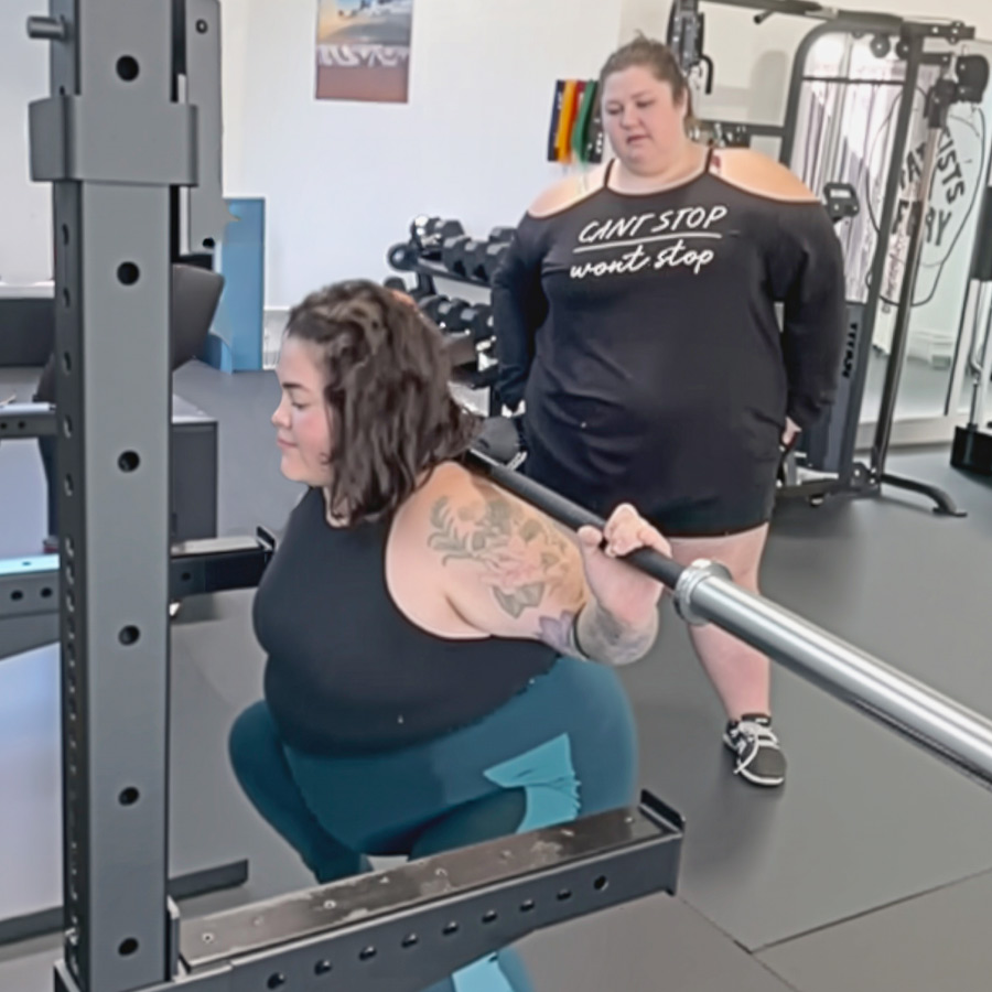 Coach Christina watching over a client as they squat.