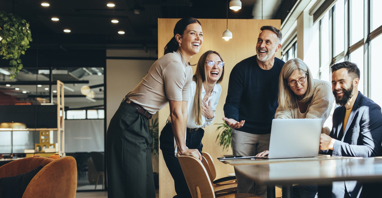 Diverse team celebrating around a laptop in a modern office