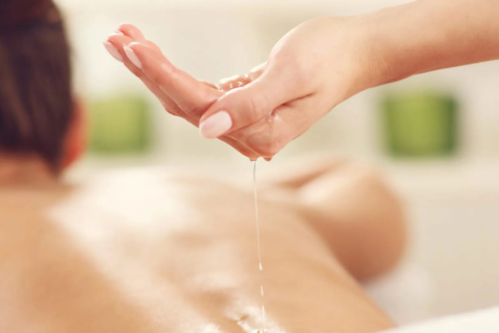 Hand pouring massage oil onto a person's bare back during a spa treatment.