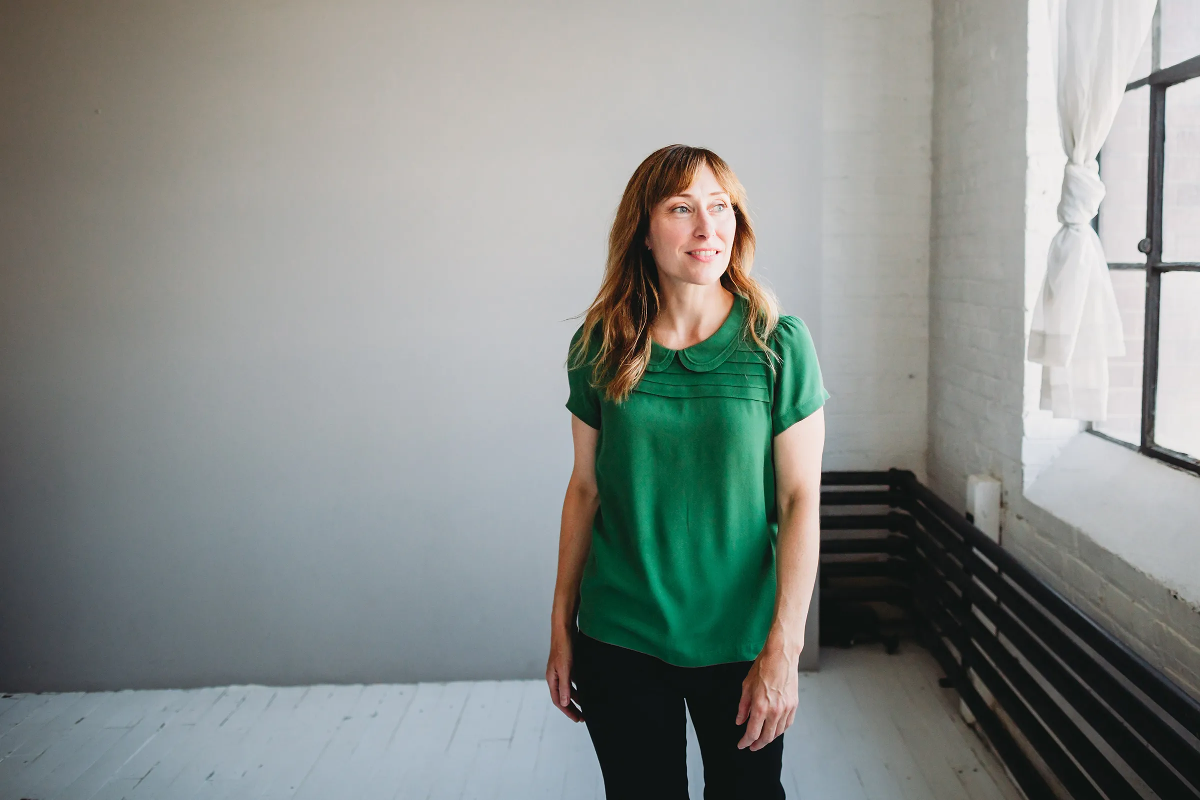 Inger Johnson, licensed acupuncturist and Traditional Easter medicine with wearing a green blouse looking out a large window in a bright, minimalist room.