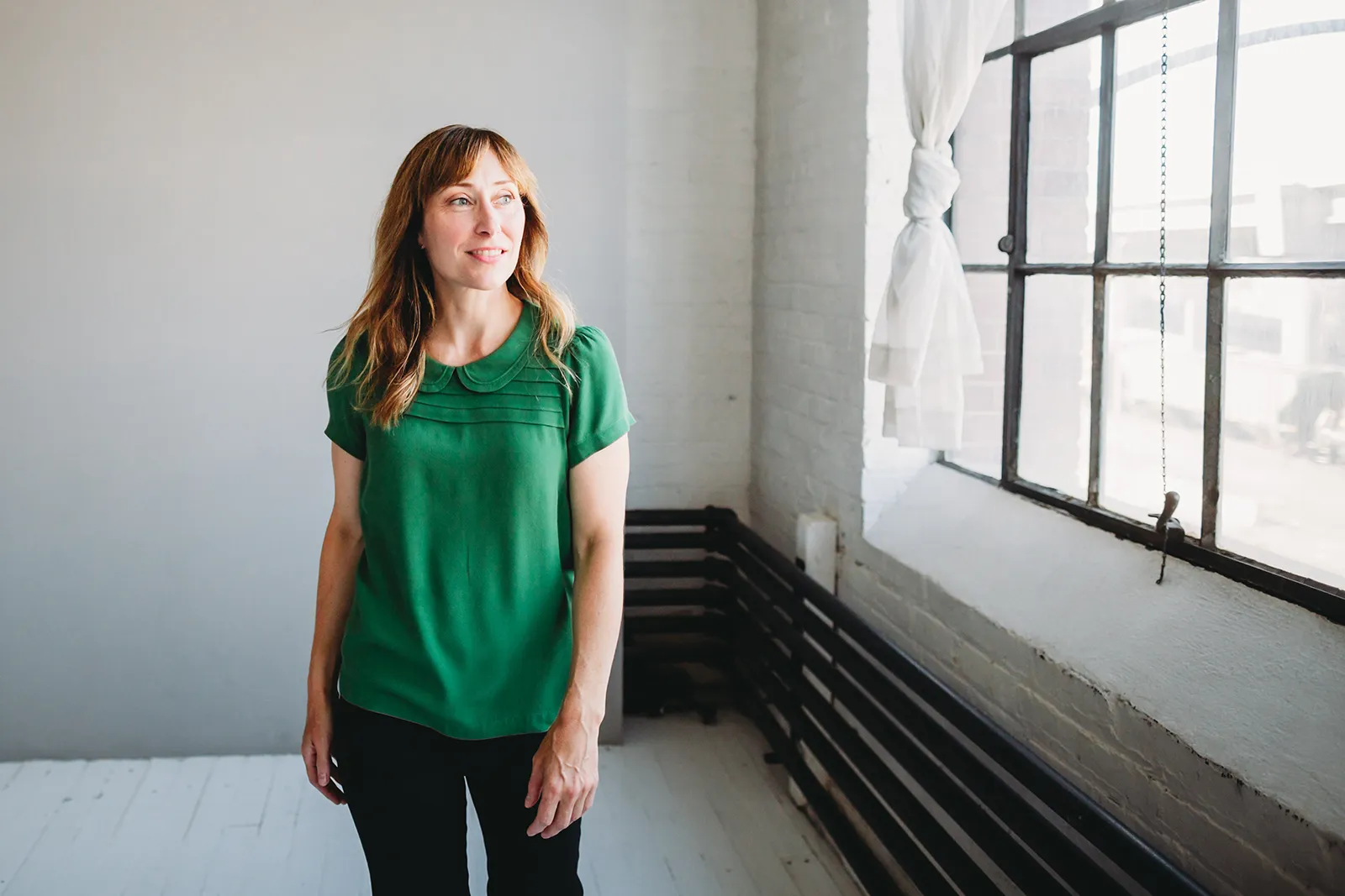 Inger Johnson, licensed acupuncturist and Traditional Easter medicine with wearing a green blouse looking out a large window in a bright, minimalist room.