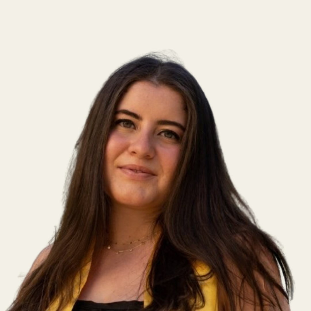 Young woman with long dark hair smiling softly, wearing a yellow outfit against a plain light background.