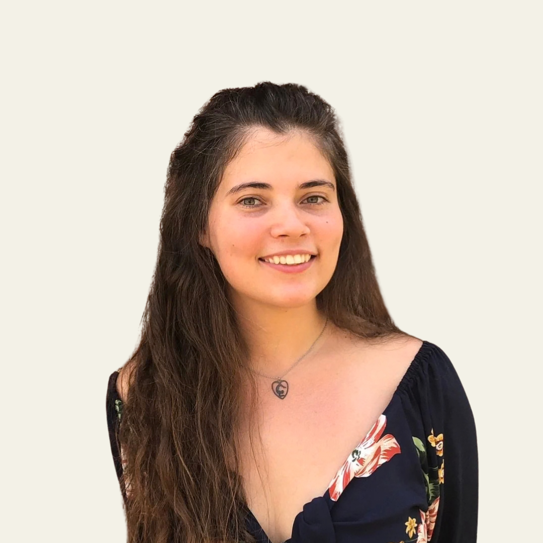 Smiling young woman with long dark hair wearing a floral off-shoulder top and a pendant necklace.