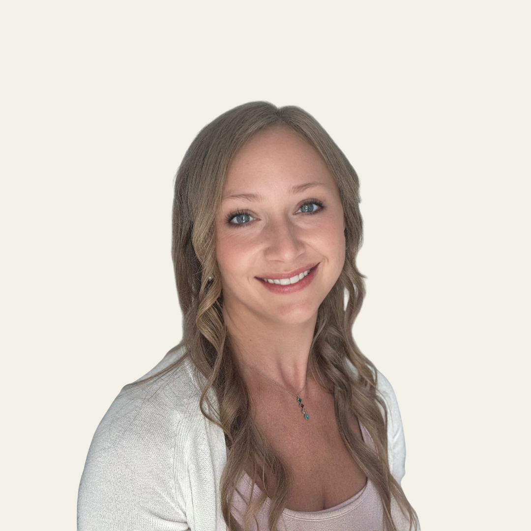 Portrait of a smiling woman with long wavy blonde hair, wearing a white cardigan and a pink top against a light background.