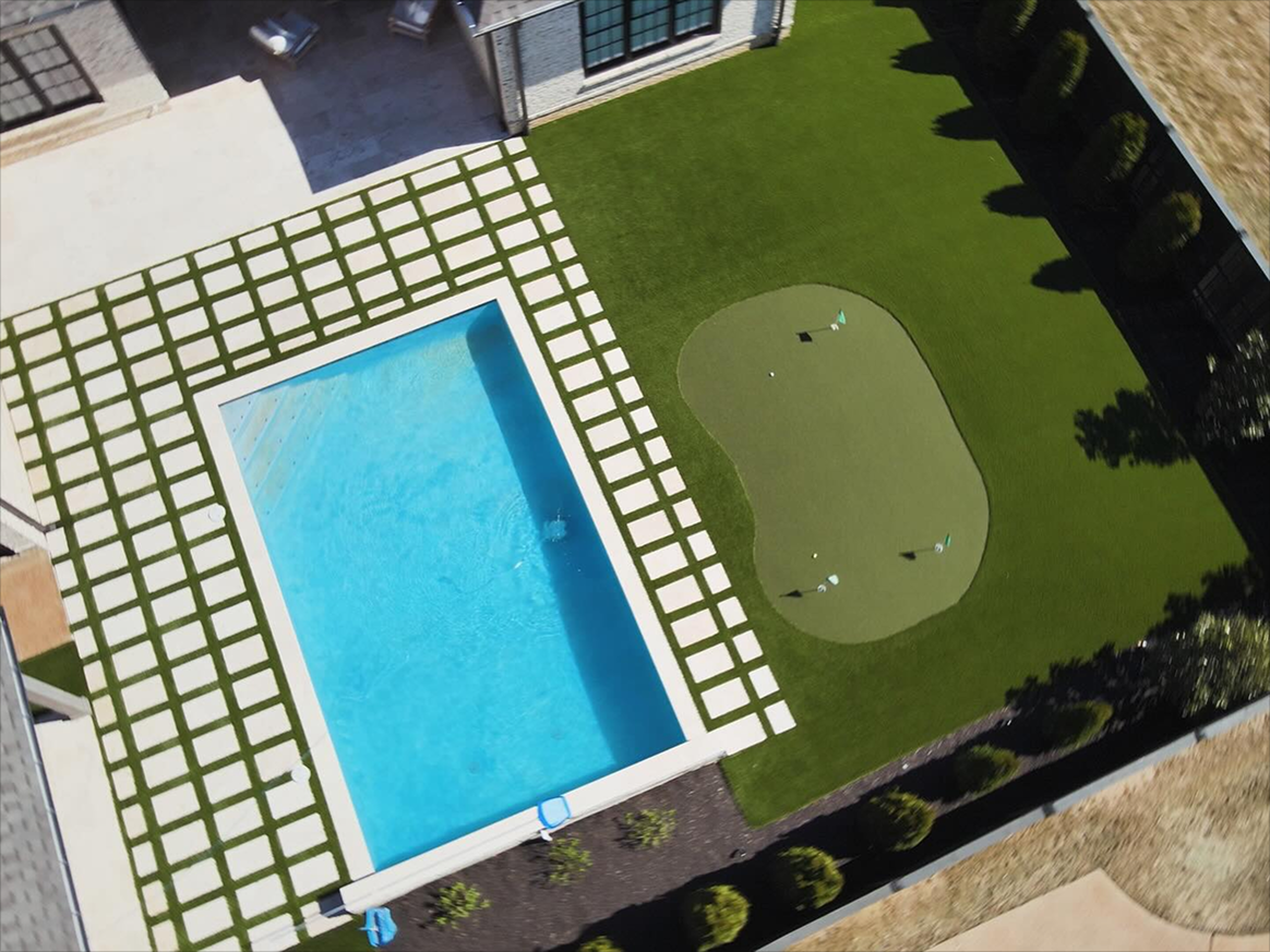 Backyard with a rectangular swimming pool surrounded by grass and a small putting green next to it.