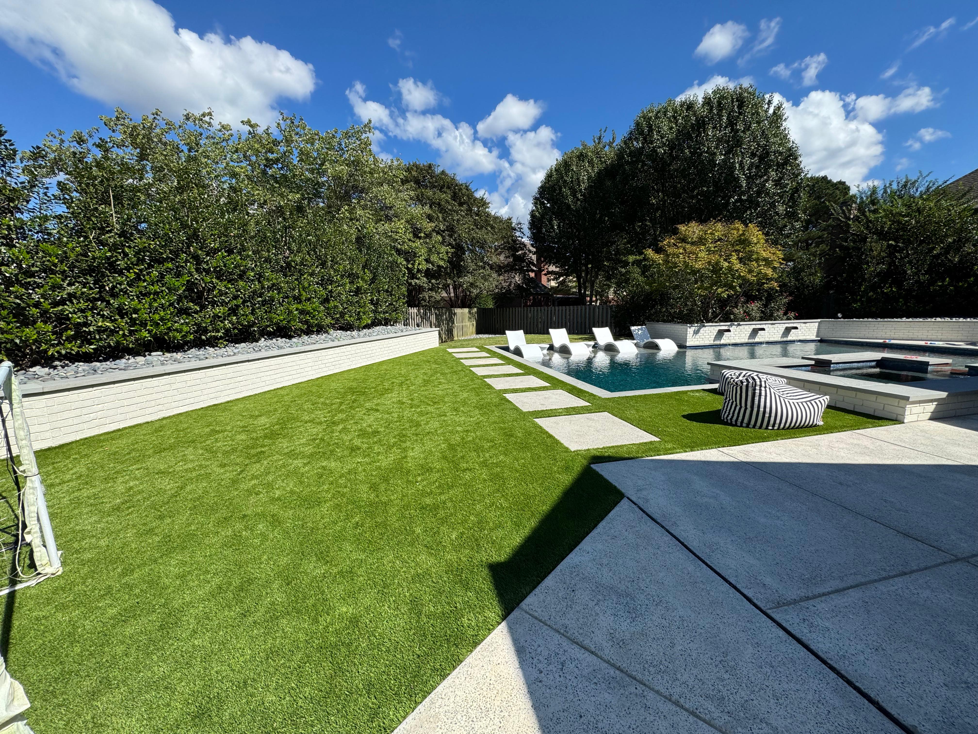 Backyard with artificial grass, stone path, pool with four lounge chairs, and a striped bean bag chair.