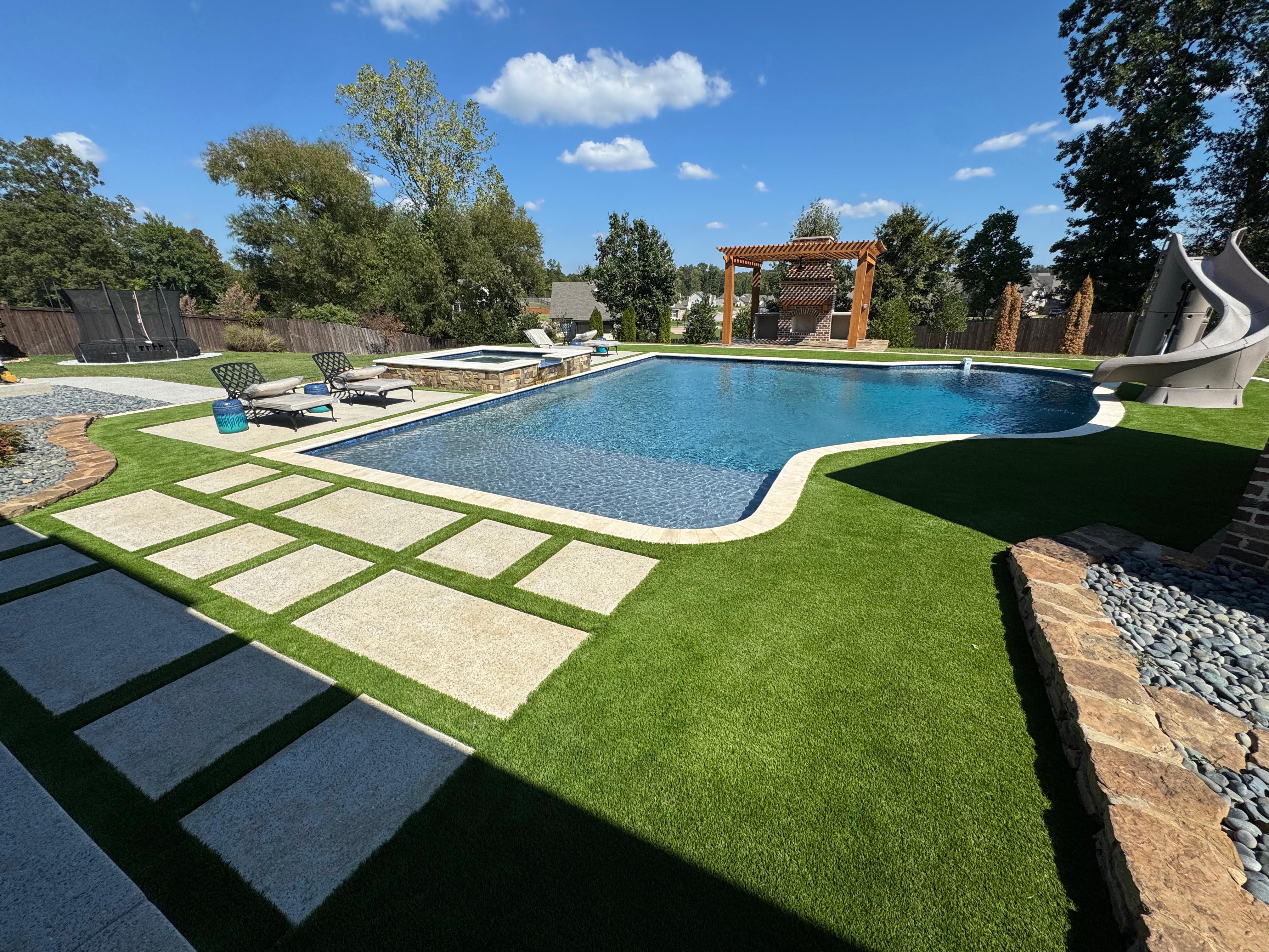 Outdoor pool with stone hot tub, lounge chairs, slide, and pergola in landscaped backyard.