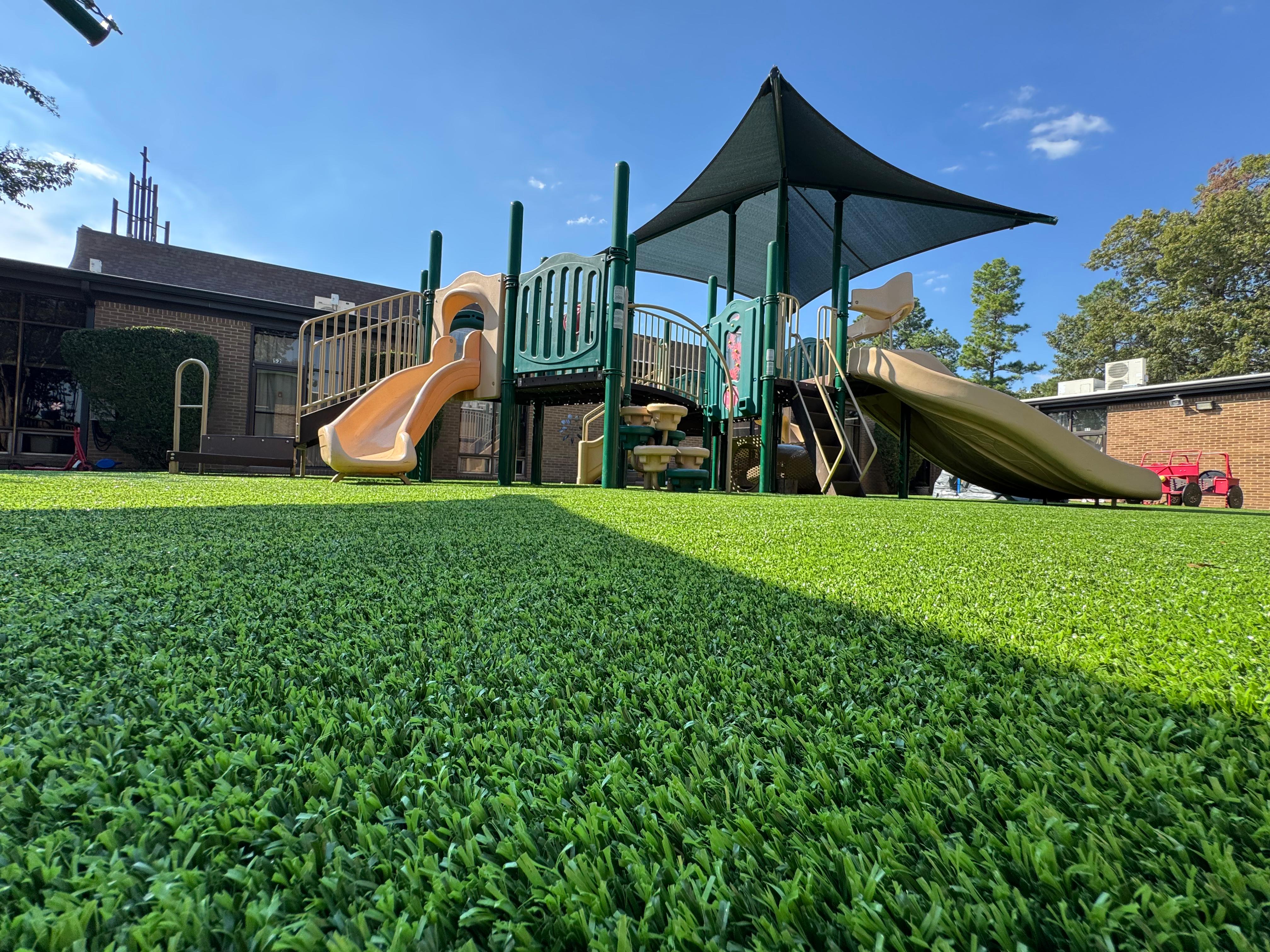 Playground with slides and climbing structures on green artificial grass under blue sky.