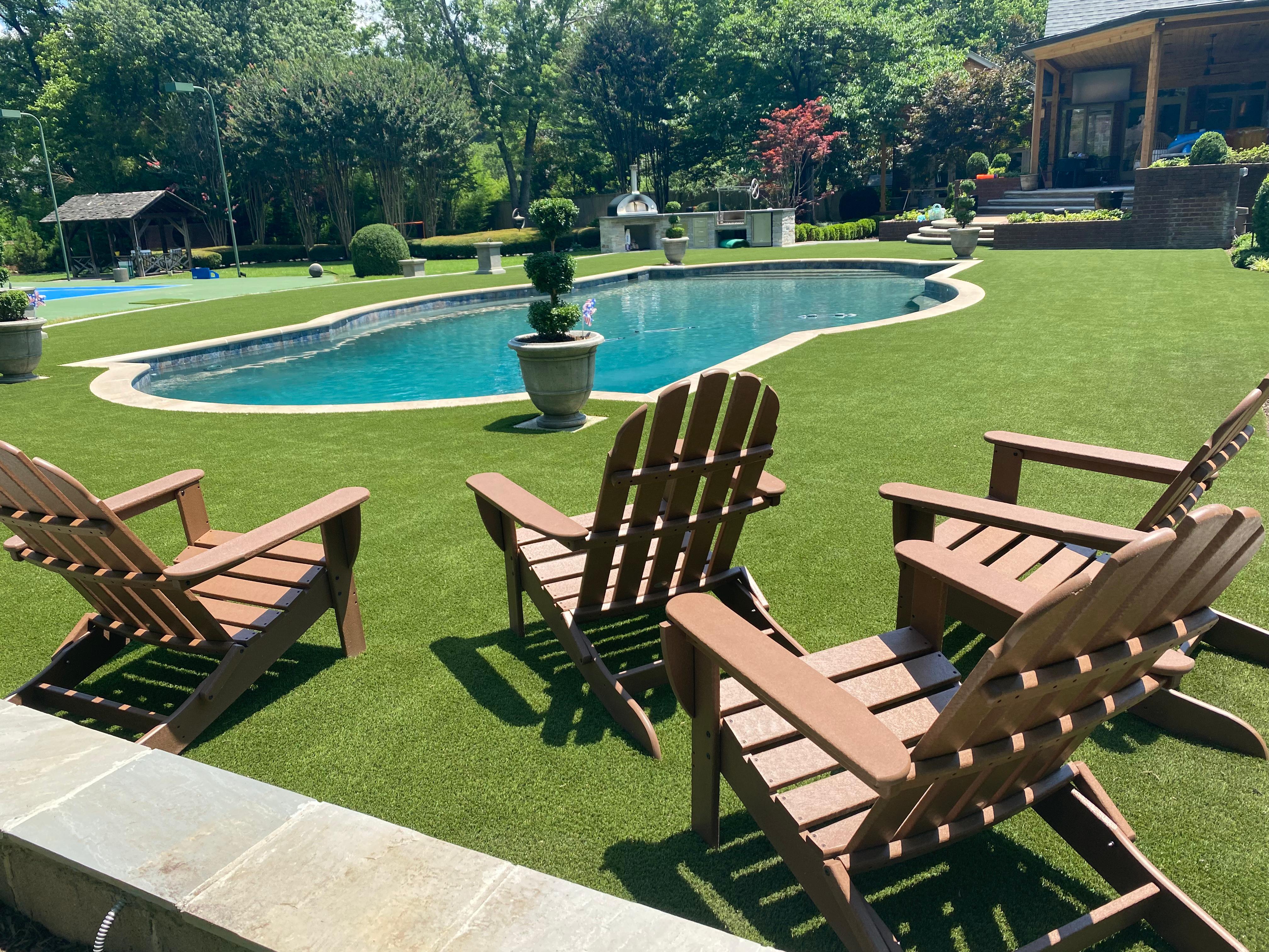 Backyard with four brown Adirondack chairs around kidney-shaped swimming pool on green lawn.