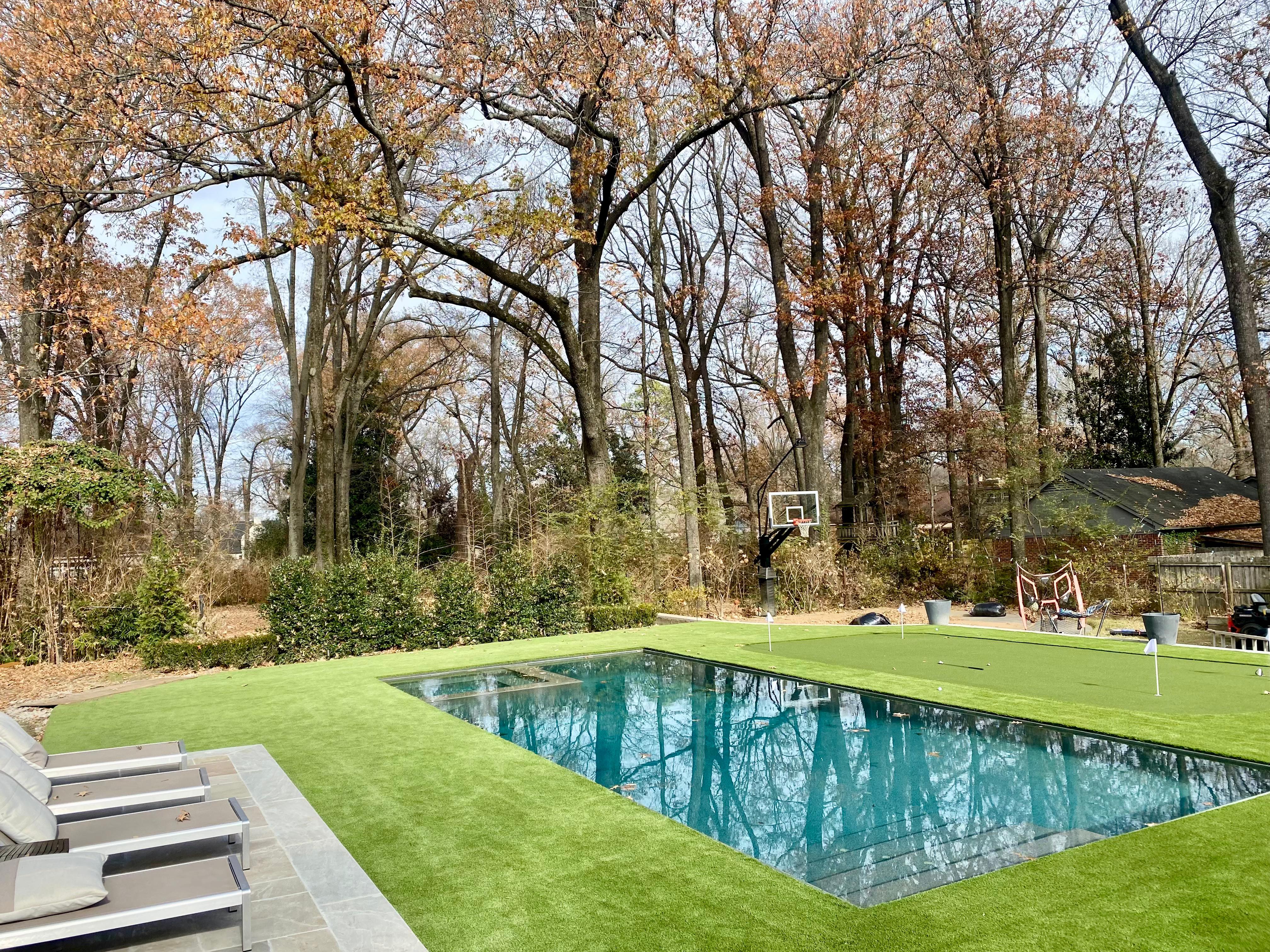 Backyard with a rectangular pool, putting green, basketball hoop, and lounge chairs on stone patio.