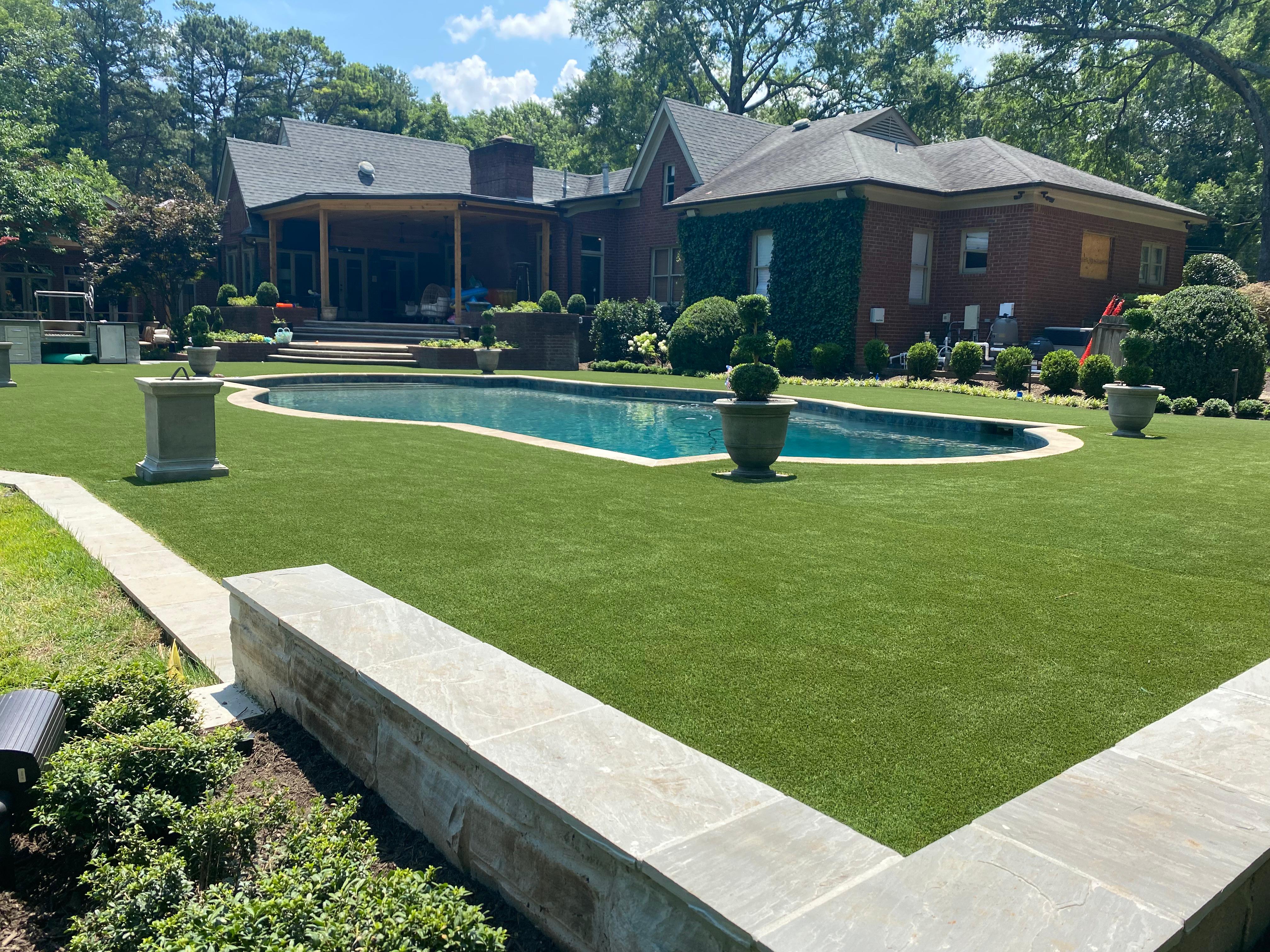Backyard with a kidney-shaped pool surrounded by green lawn and a brick house in the background.