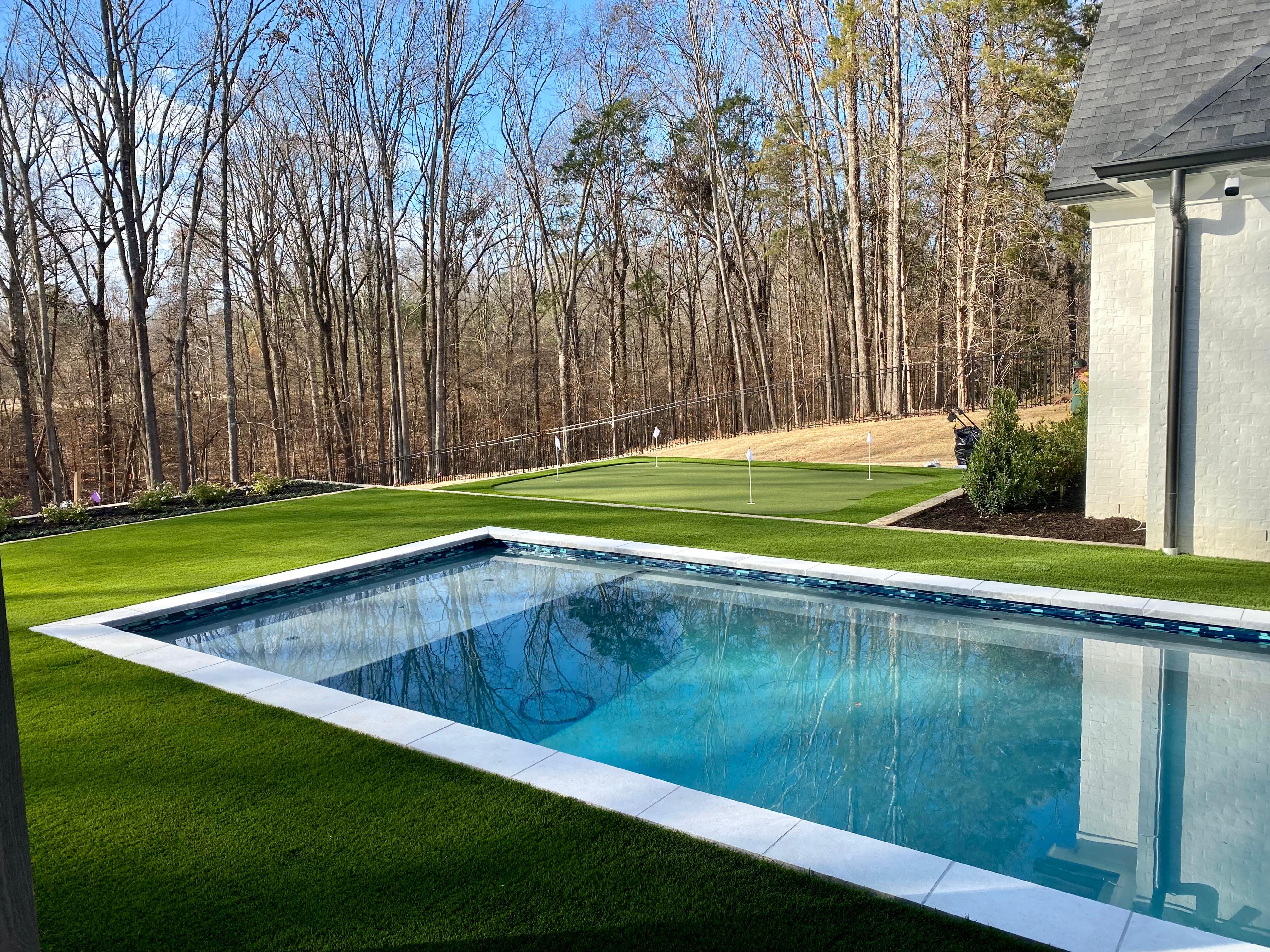 Rectangular pool in backyard with artificial grass surrounds and golf putting green in the background.
