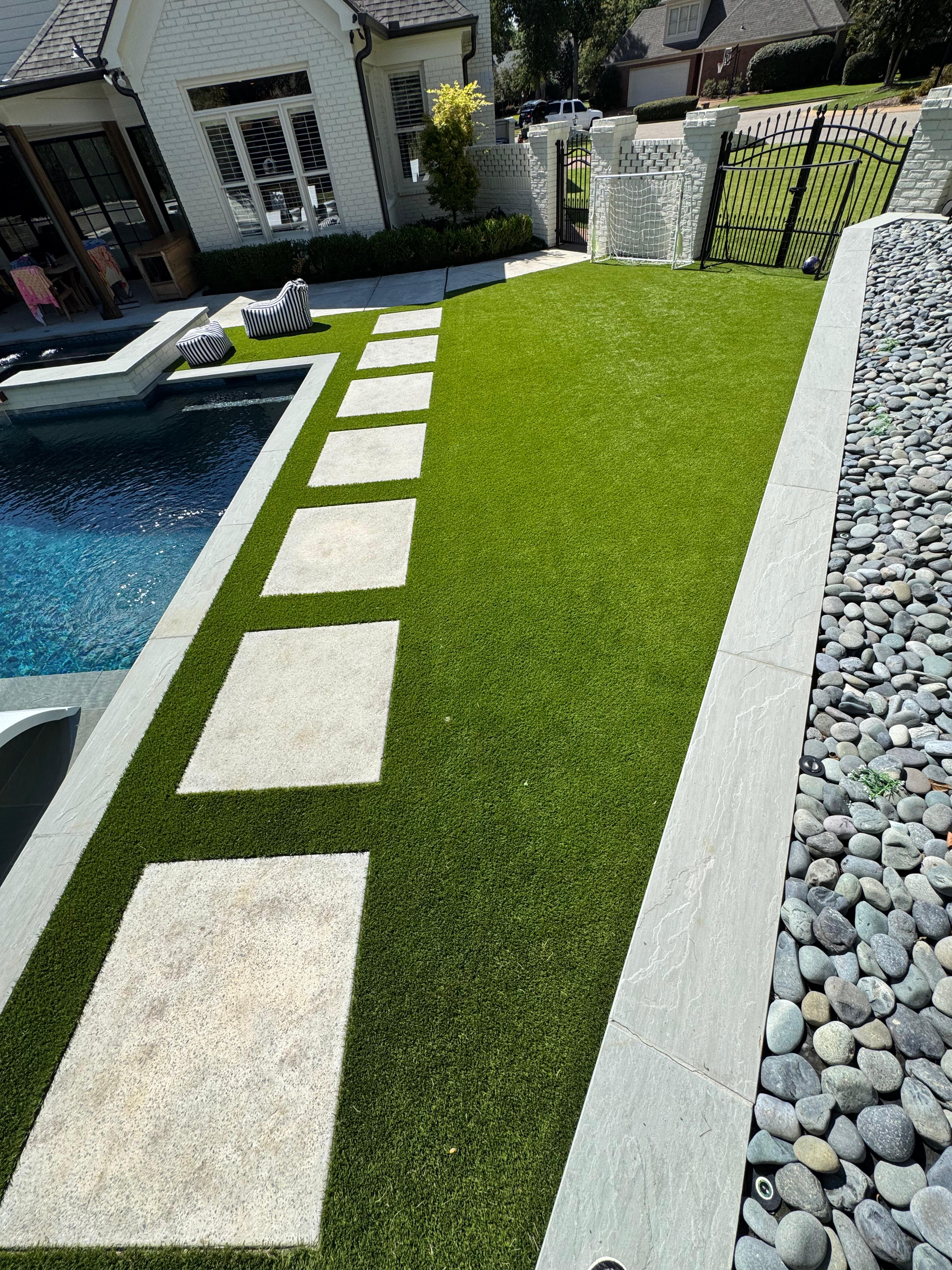 Backyard with artificial turf, stone stepping path, pool, outdoor chairs, and a small soccer goal.