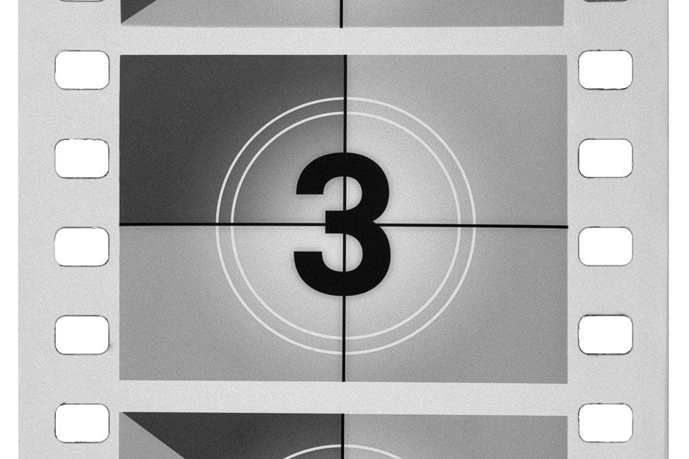 Close-up of black and white vintage filmstrip showing a countdown frame with the number 3 centered inside two concentric circles and crosshair marks.